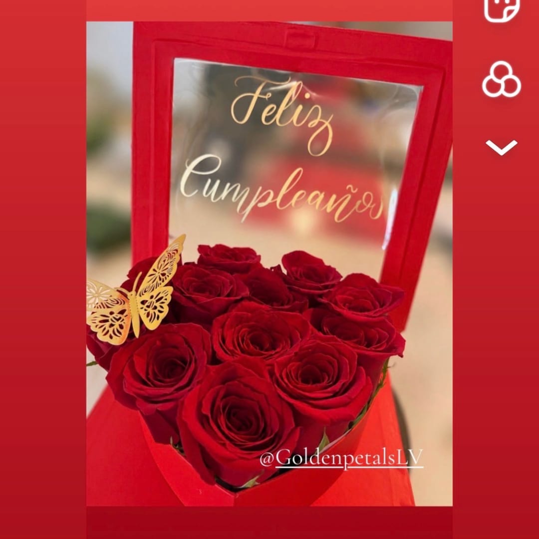 Red roses in a red gift box with a butterfly decoration and "Feliz Cumpleaños" text.