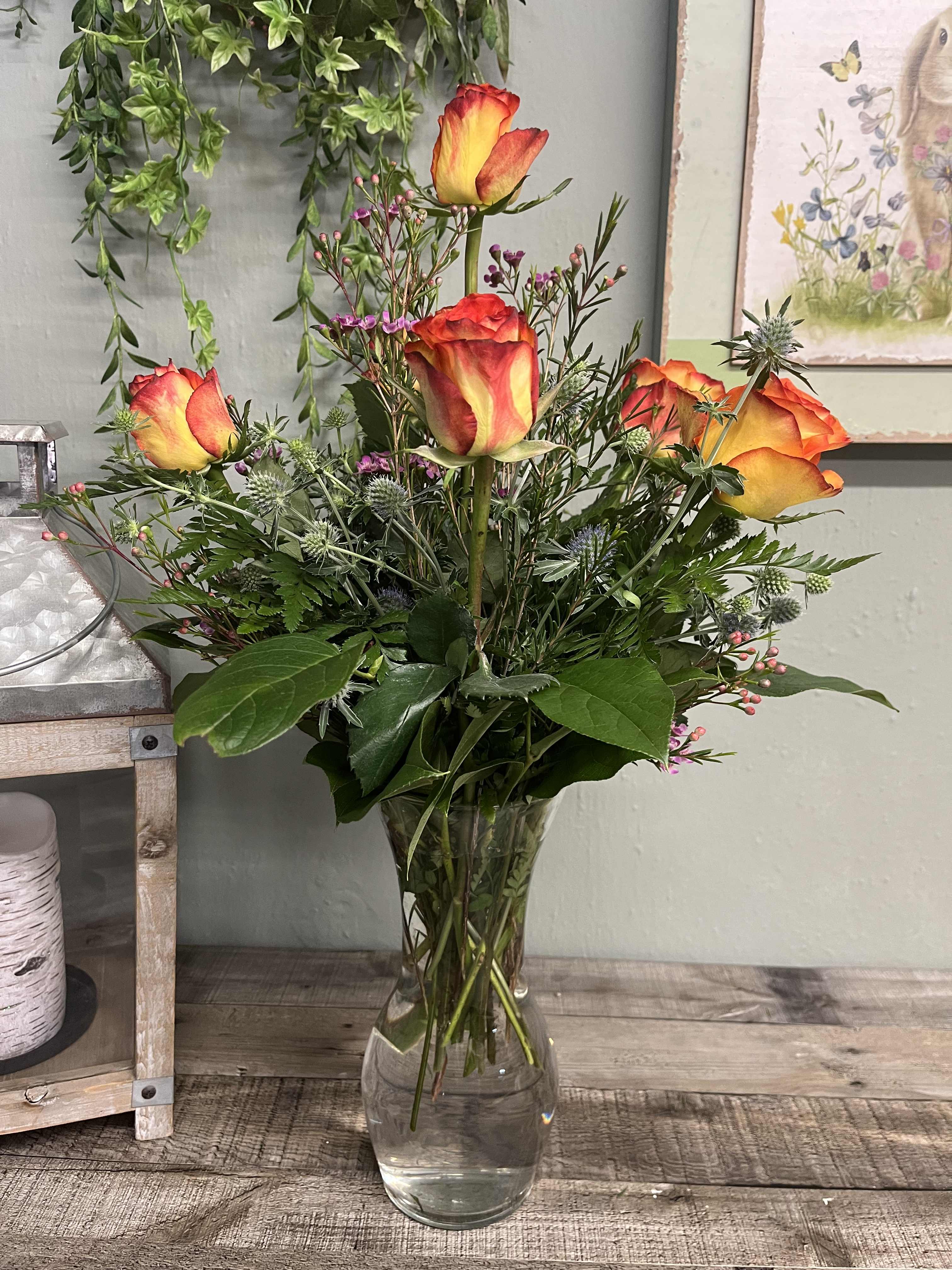 Orange-yellow roses in a clear glass vase with mixed greenery
