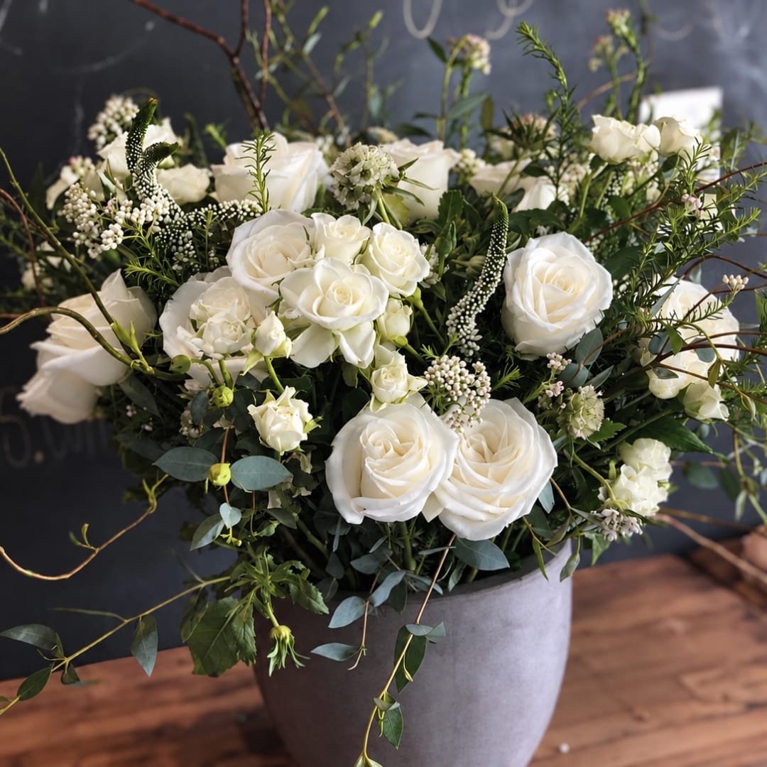 White roses and small white blooms arranged in a gray vase