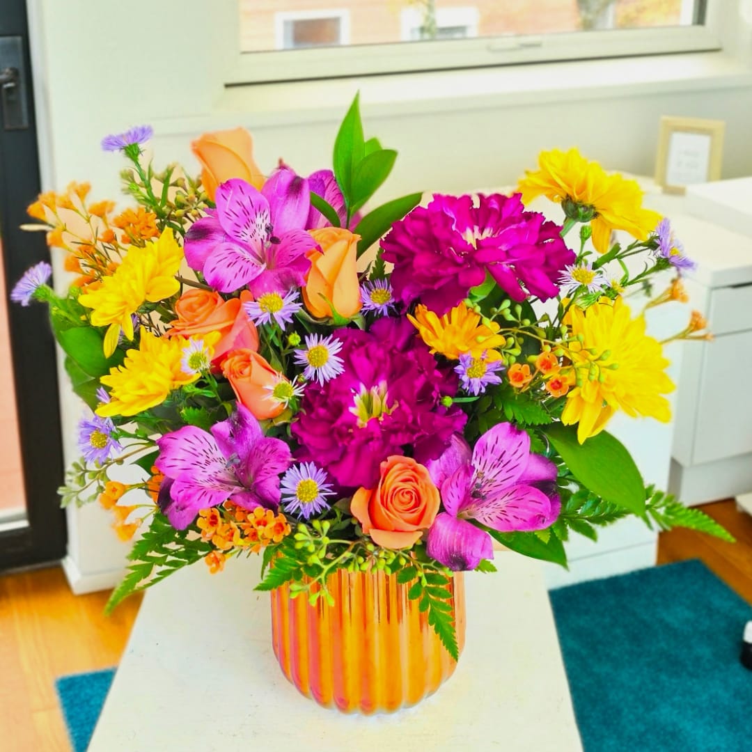 Bright mixed bouquet in a striped glass vase with pink, orange, and yellow blooms.