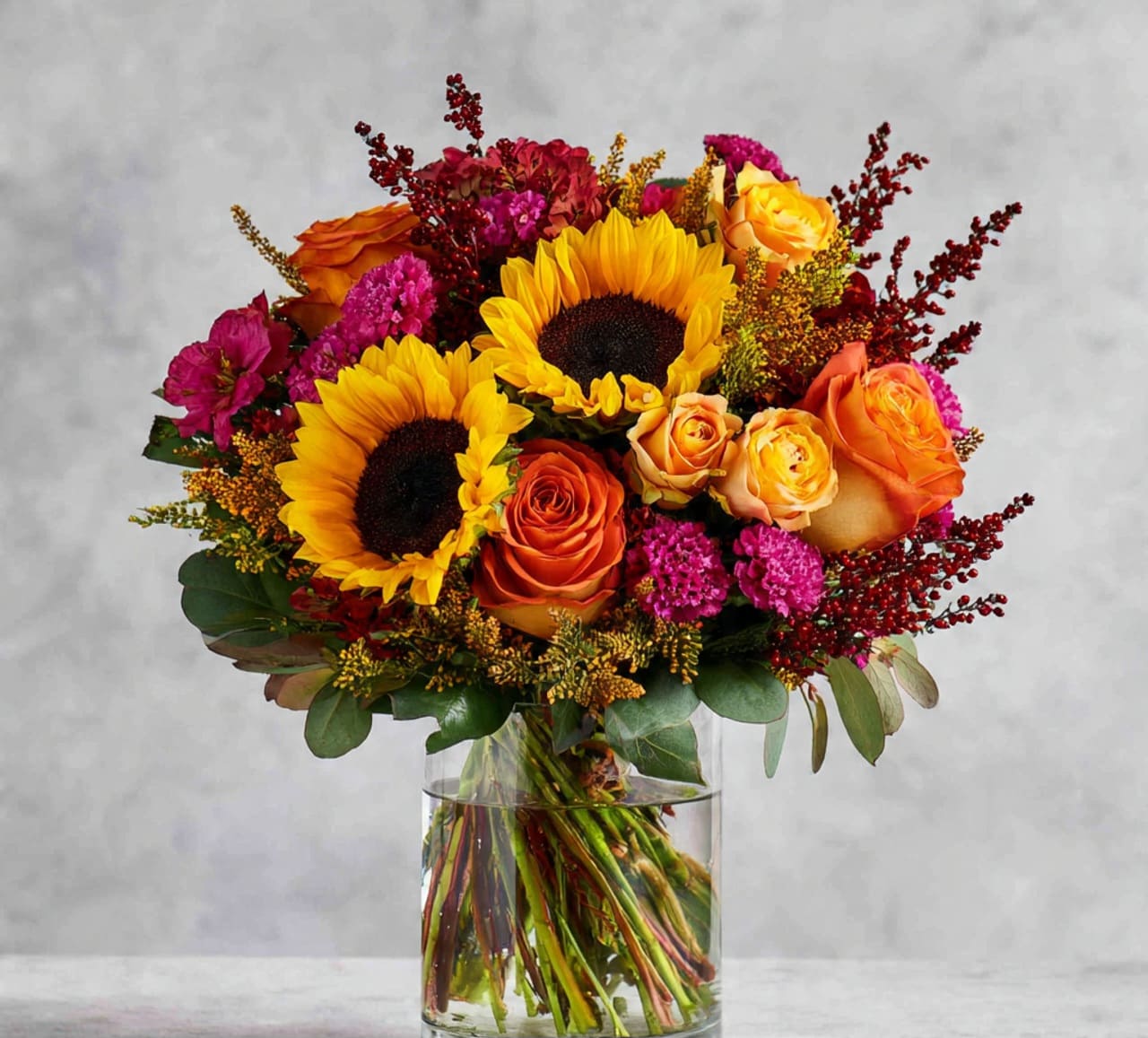 Bouquet of sunflowers and orange roses in a clear glass vase