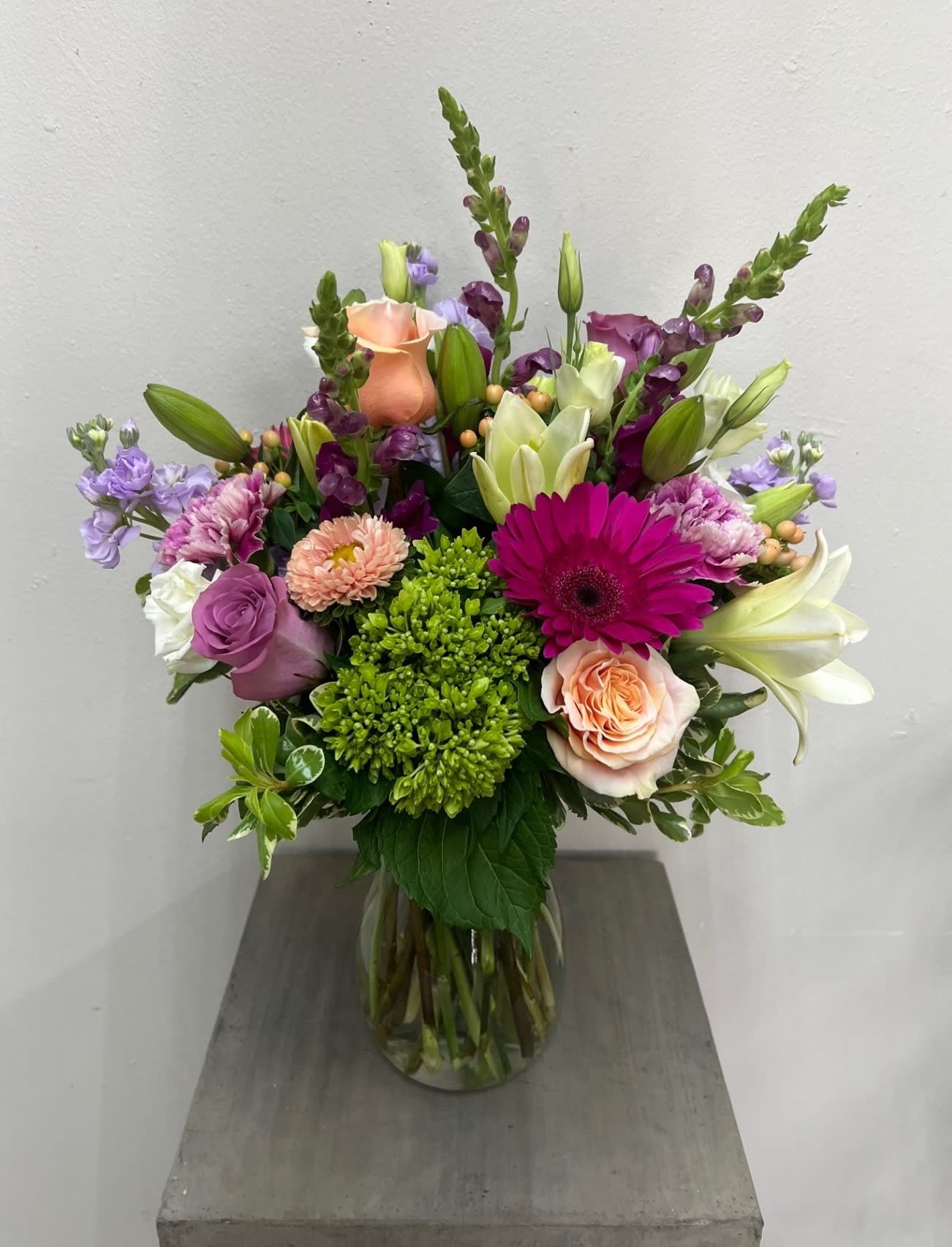 Mixed bouquet in a glass vase with roses, lilies, and purple blooms