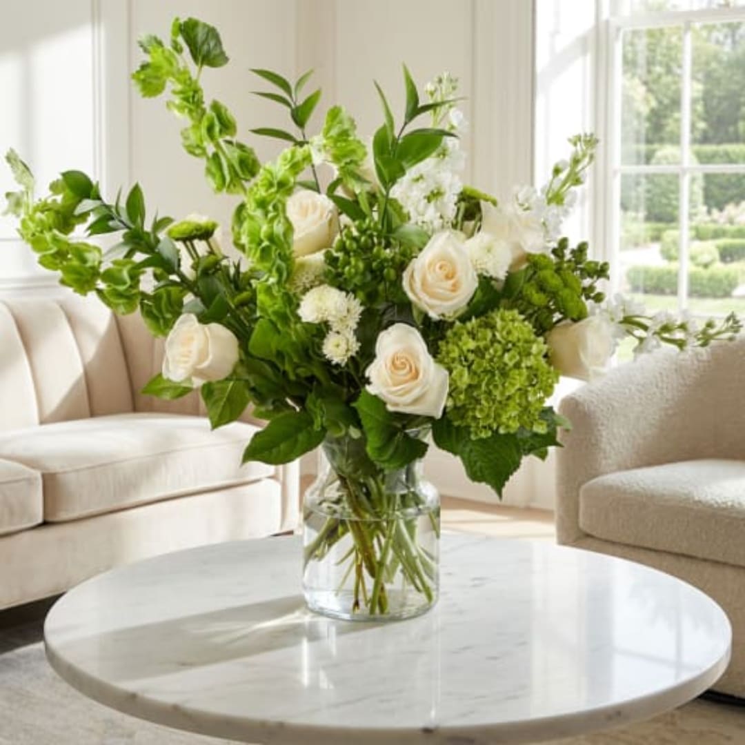 White roses and green flowers in a clear glass vase on a table