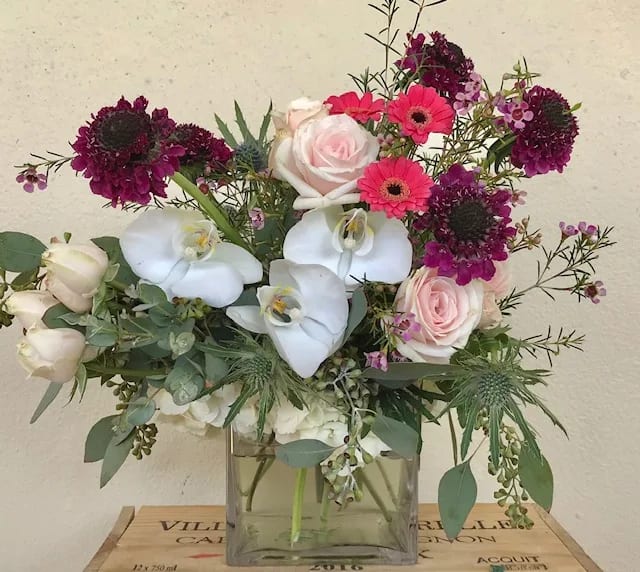 Mixed bouquet with pink roses, white orchids, and magenta blooms in a glass vase