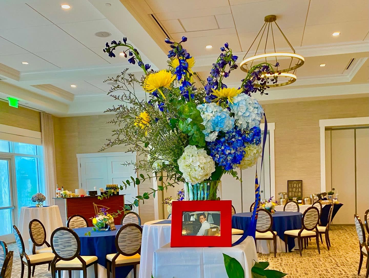 Tall floral centerpiece with blue, yellow, and white blooms in a vase