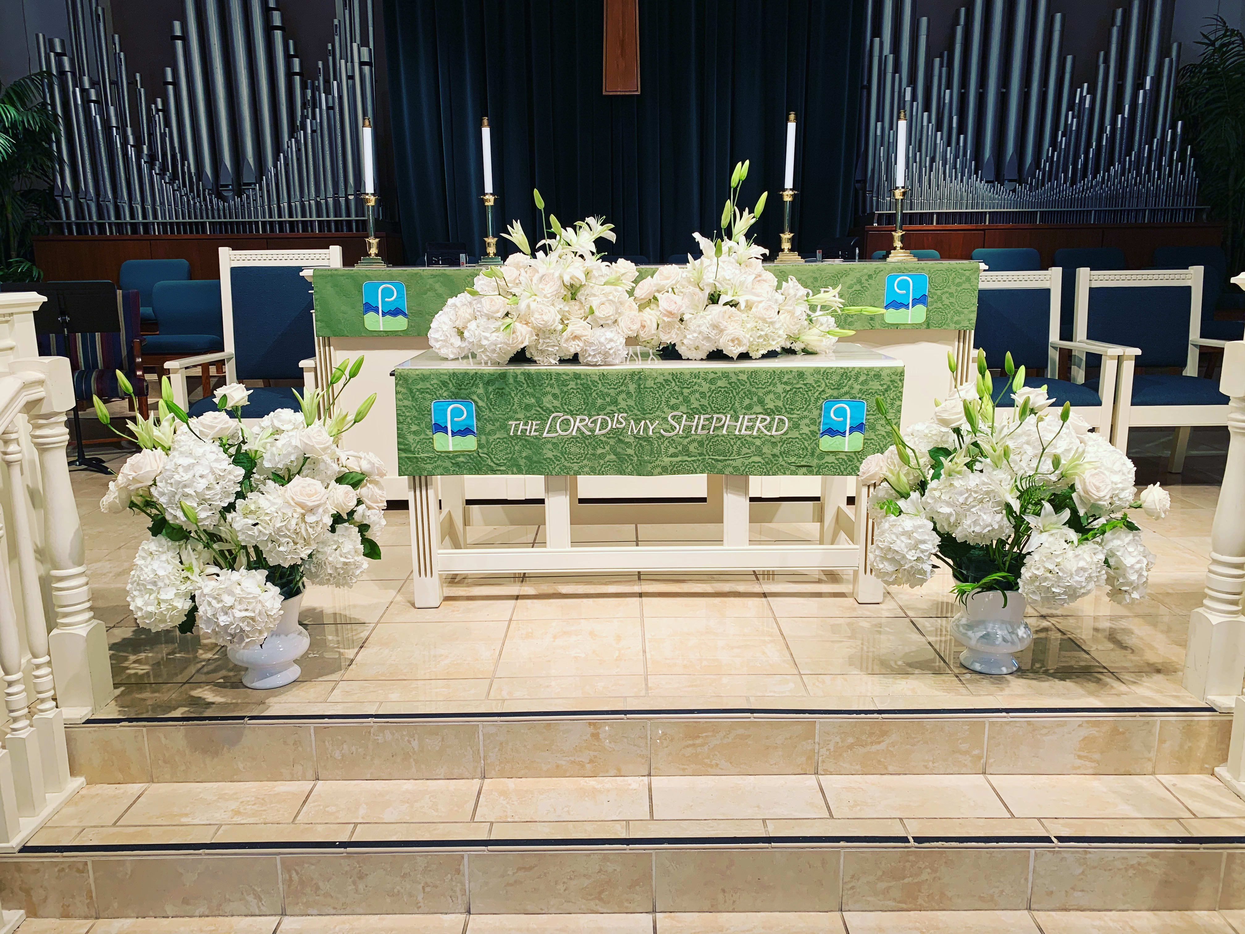 White floral altar arrangements in a church with green altar cloths