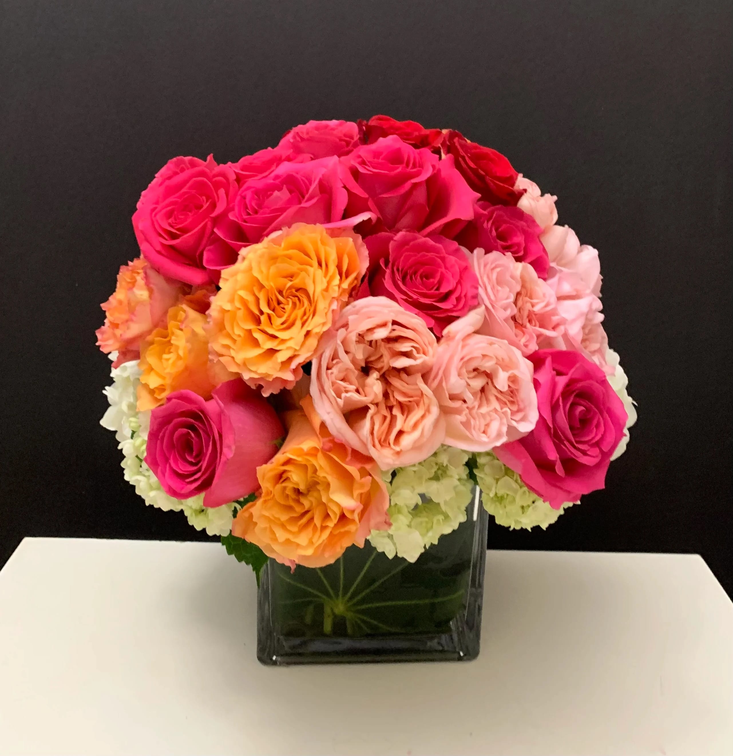 Bouquet of pink, peach, and orange roses in a square glass vase