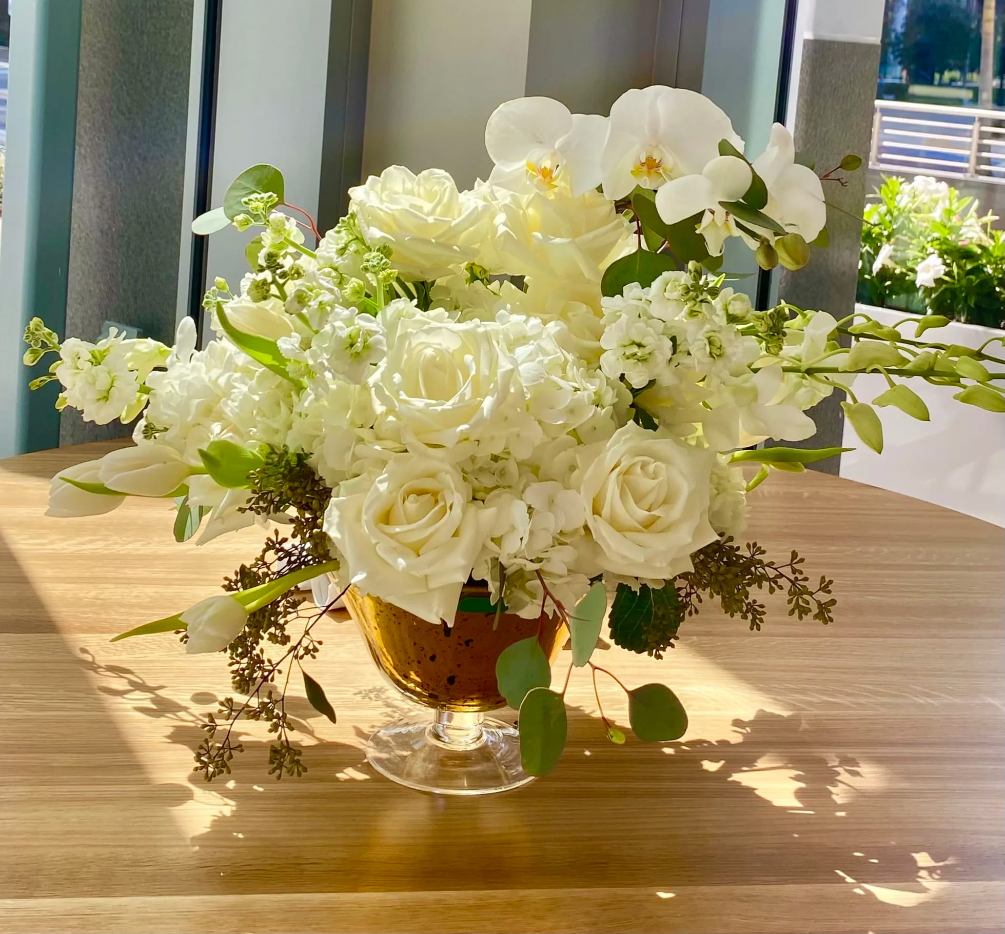 White roses and orchids arranged in a glass compote vase