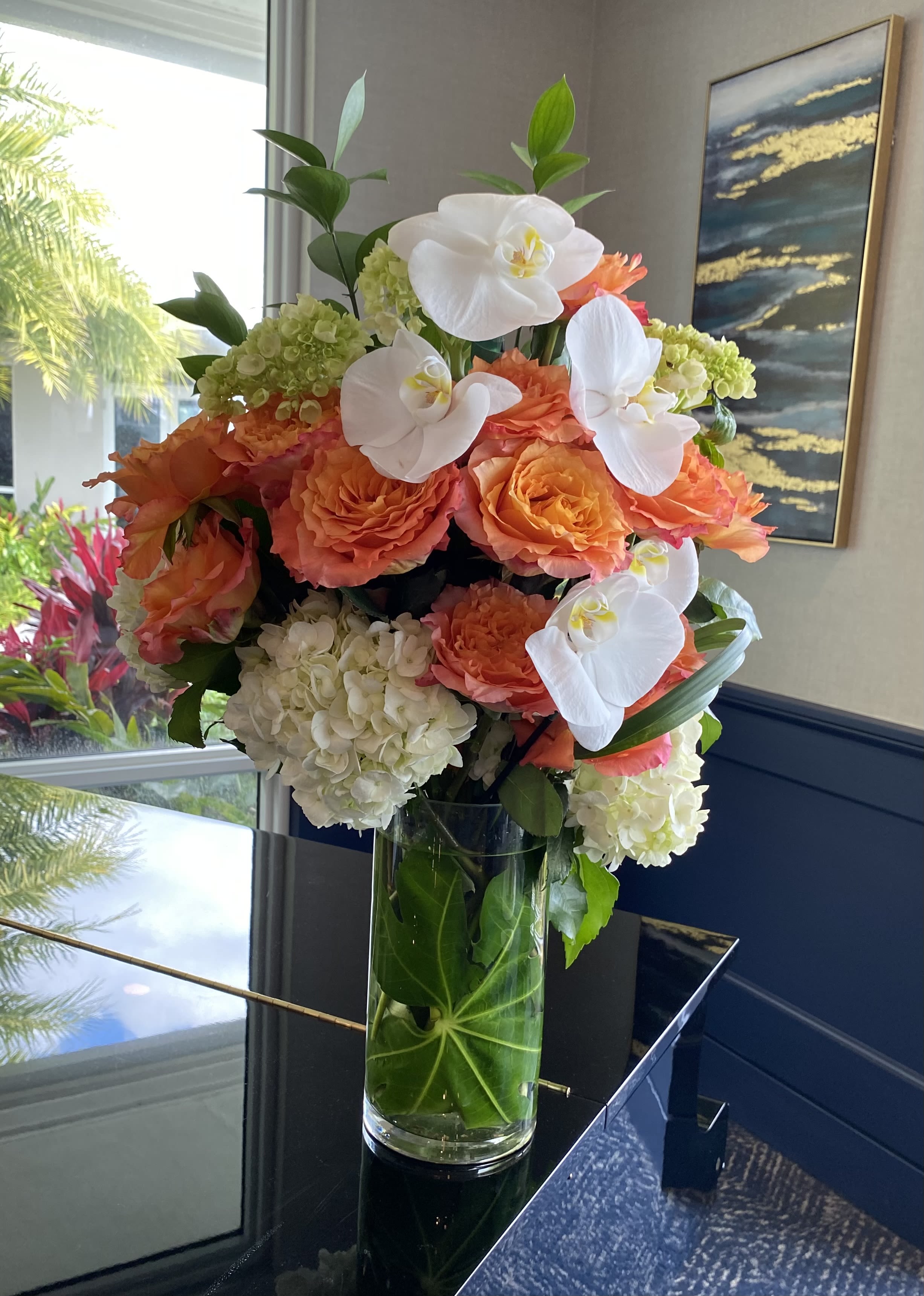 Orange roses and white orchids arranged in a tall glass vase