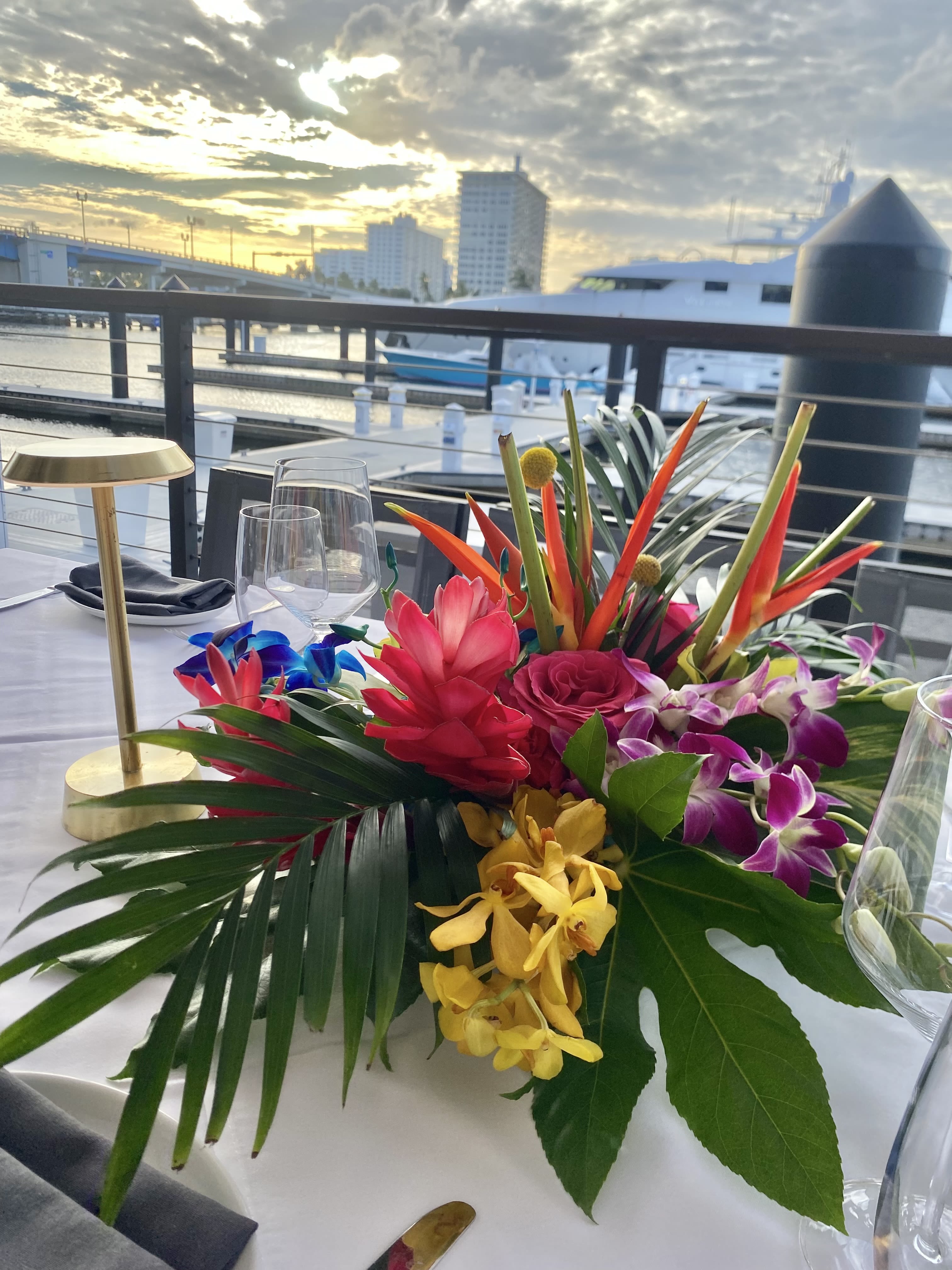 Tropical floral centerpiece with orchids, roses, and bright red blooms