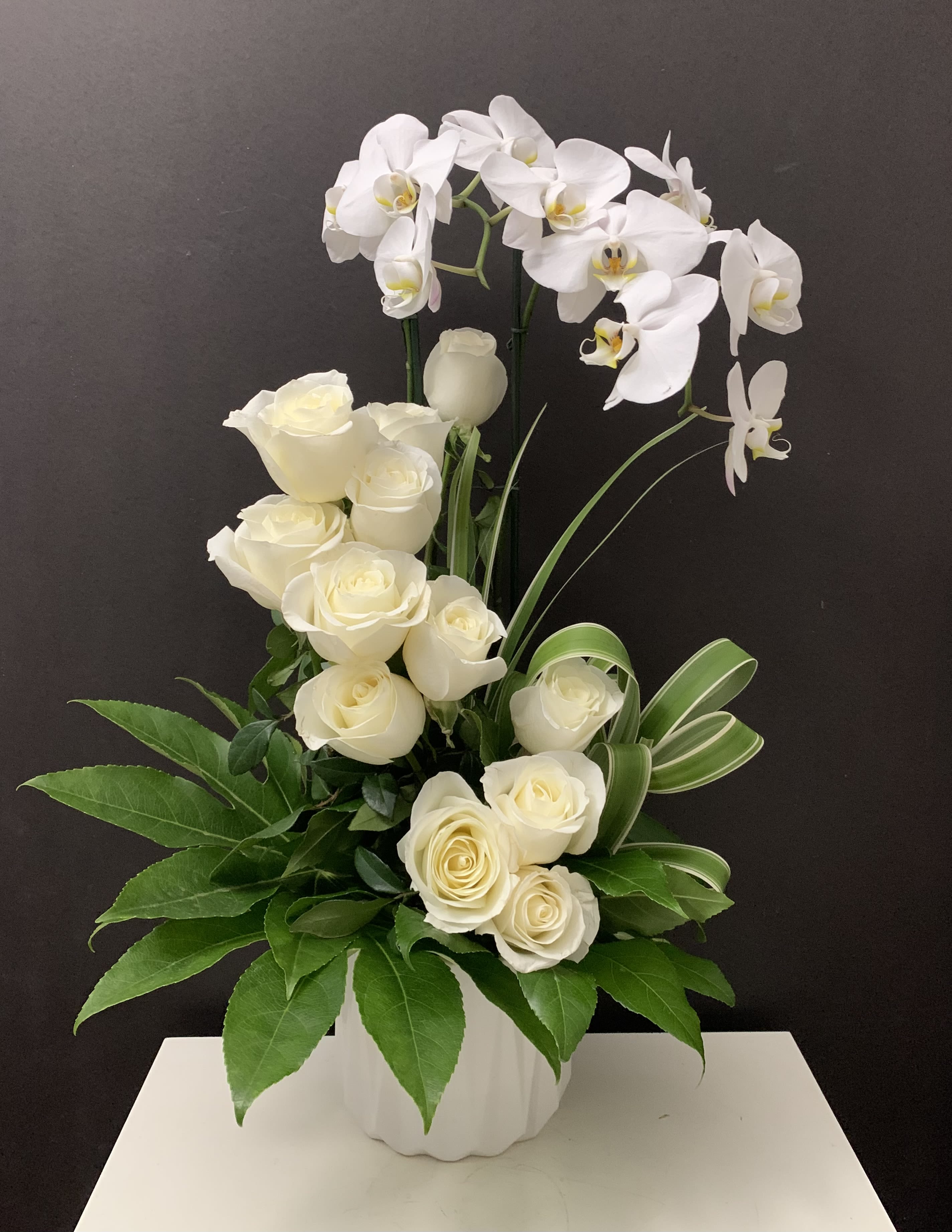 White roses and orchids arranged in a white vase