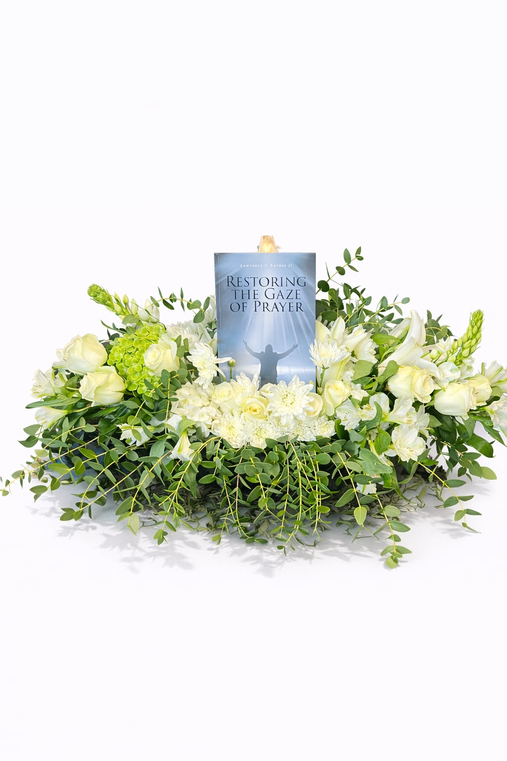 Urn Sympathy Tribute - Serene, meaningful, and beautifully composed, this elegant arrangement blends soft white roses, hydrangeas, and delicate blooms with lush flowing greenery, creating a peaceful and comforting presence.  Designed with a central space to hold a meaningful item—such as a book, photo, or candle—this piece becomes more than flowers; it becomes a tribute filled with love, faith, and remembrance. The soft white tones symbolize peace and purity, while the natural greenery represents life, renewal, and eternal connection.  Perfect for memorials, celebrations of life, or spiritual gatherings, this arrangement offers a graceful way to honor, reflect, and bring comfort to those who gather.  A heartfelt expression of peace, love, and remembrance.
