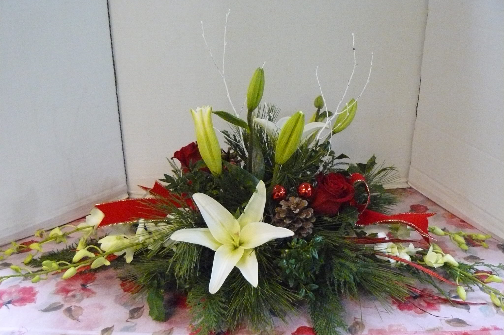 Low floral centerpiece with white lilies, red roses, and red ribbon