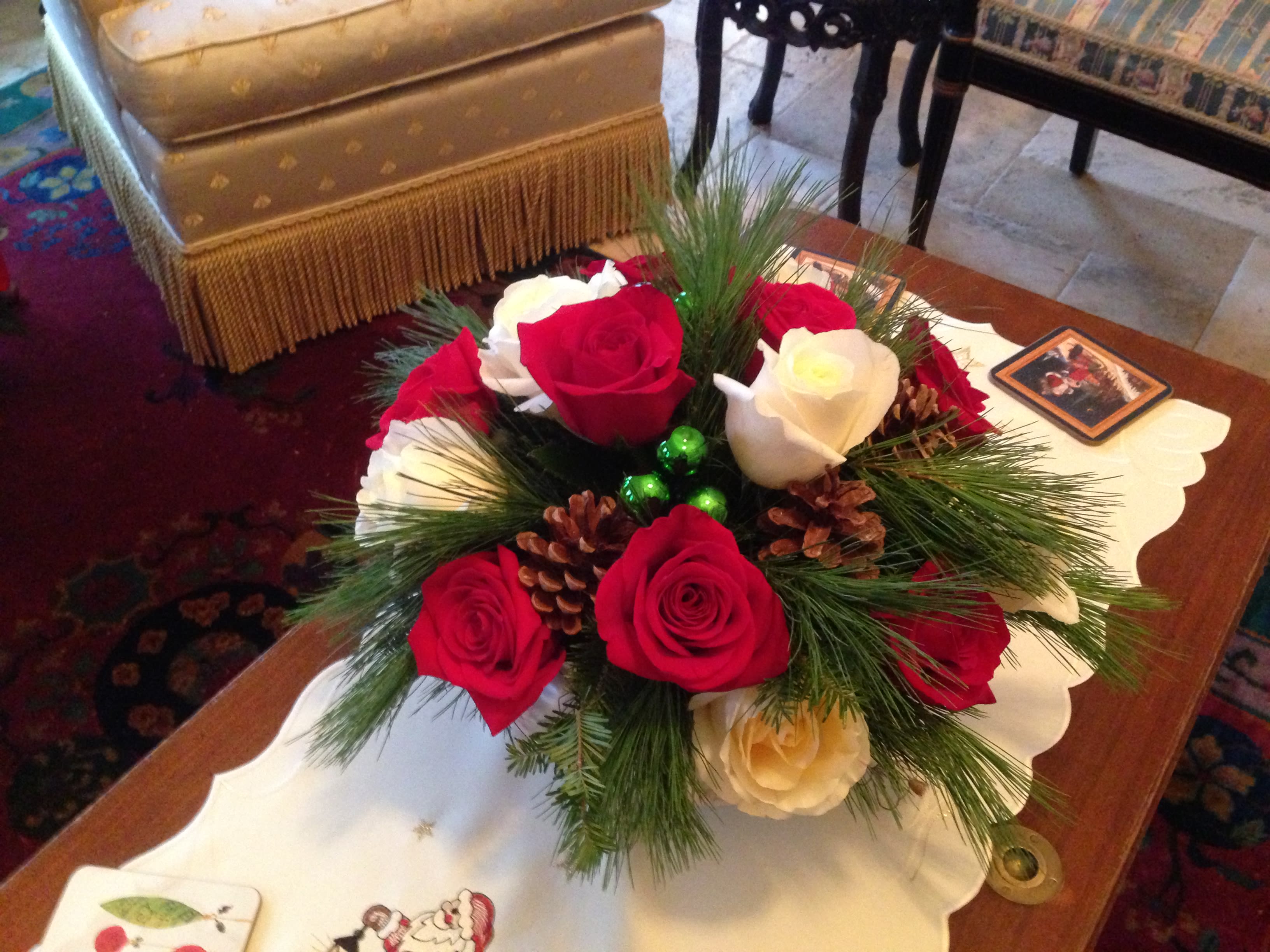 Red and white roses arranged with pine and pinecones in a low centerpiece