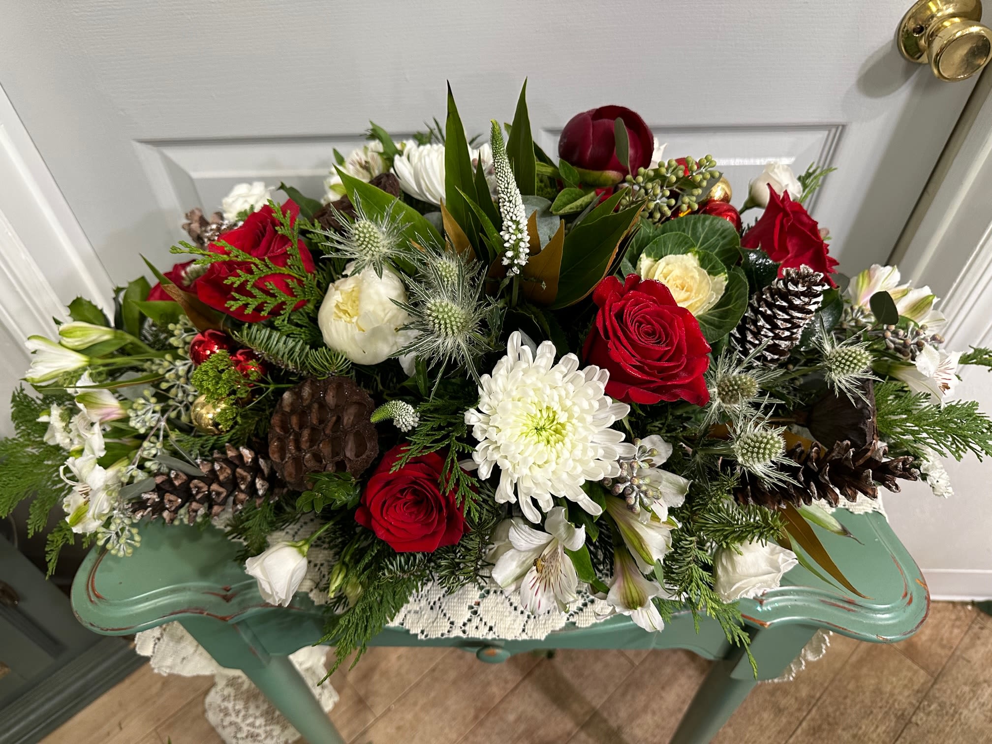 Red and white floral arrangement with pinecones in a low container
