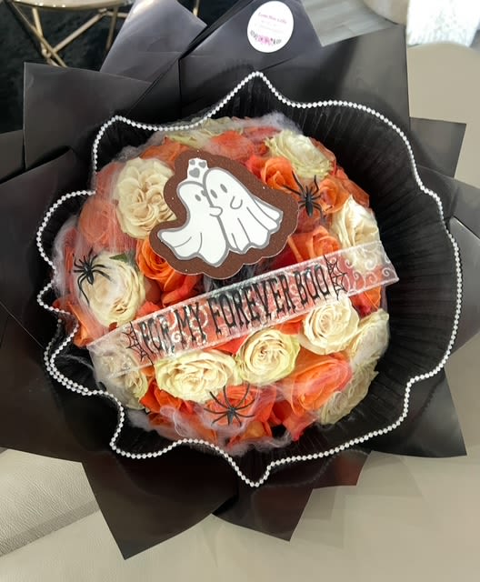 Bouquet of orange and cream roses wrapped in black paper with a ghost decoration