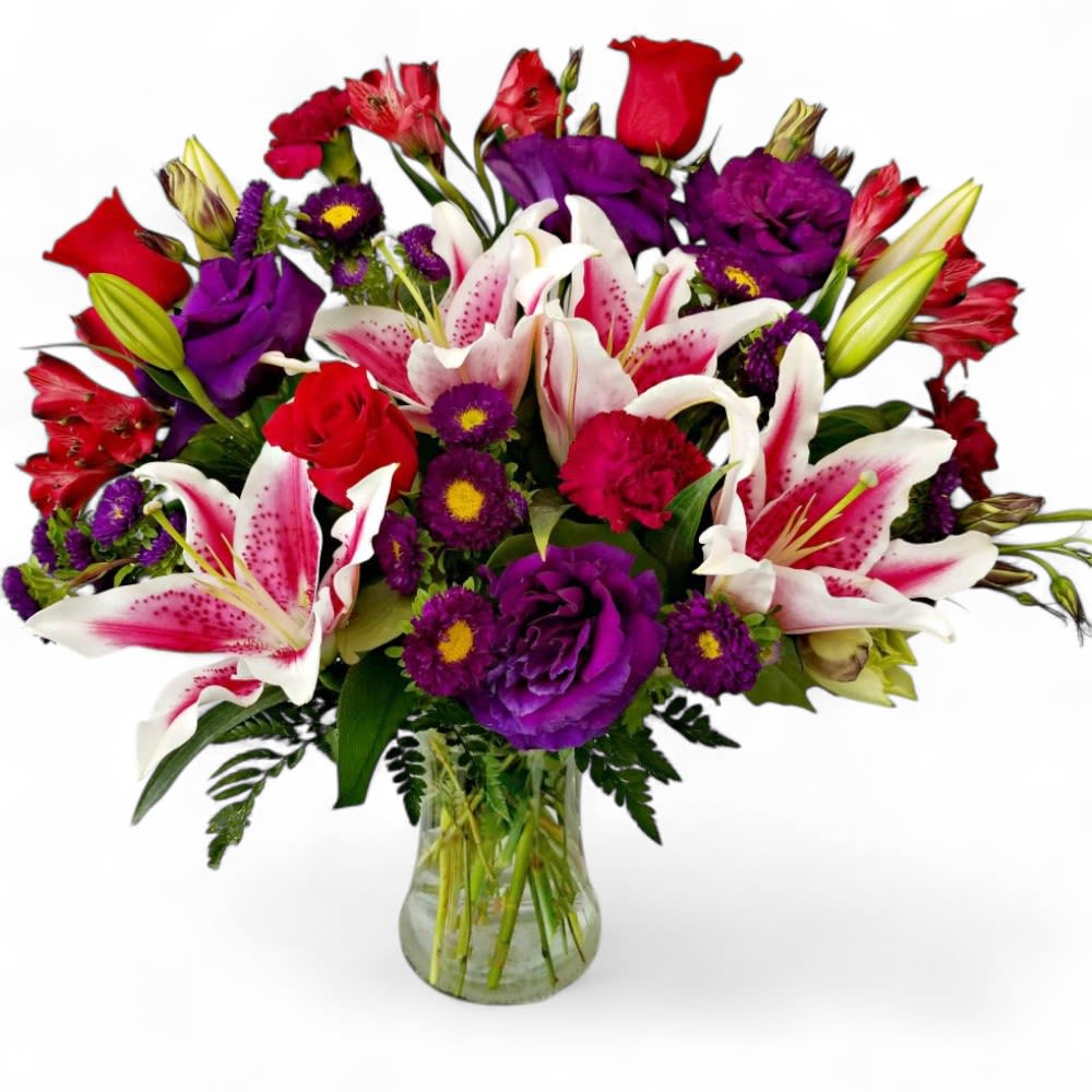 Mixed bouquet of lilies, roses, and purple flowers in a glass vase