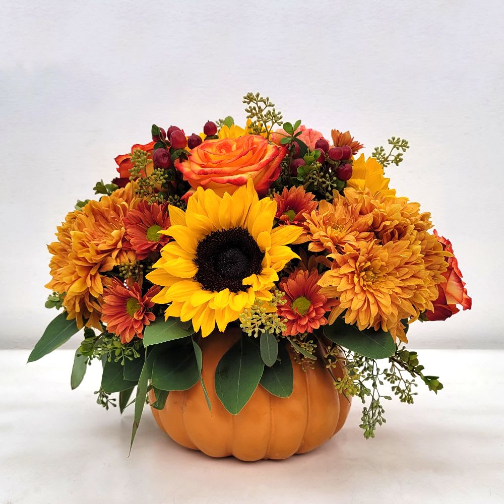 Autumn Pumpkin  - Bring the beauty of fall indoors with this stunning autumn floral arrangement, perfect for the fall season and Thanksgiving centerpieces. A variety of fresh fall flowers are artfully arranged in a charming 7-inch ceramic pumpkin container. This unique arrangement features a vibrant mix of roses, sunflowers, daisies, hypericum berries, and eucalyptus greens—all carefully selected to capture the rich colors of autumnal hues.  The warm and inviting atmosphere created by the vibrant colors and lush textures makes this a perfect addition to any home or office. It is ideal for decorating for fall, as a Thanksgiving table centerpiece, or as a thoughtful gift for a friend or loved one.  This beautiful floral arrangement is available for same-day flower delivery from Long Beach's favorite flower shop, A Beautiful California Florist. Order your Autumn Harvest Pumpkin Arrangement today to add a touch of fall magic to any space.      • Approximate size: 12" T x 12" W     • Container: 7" ceramic pumpkin