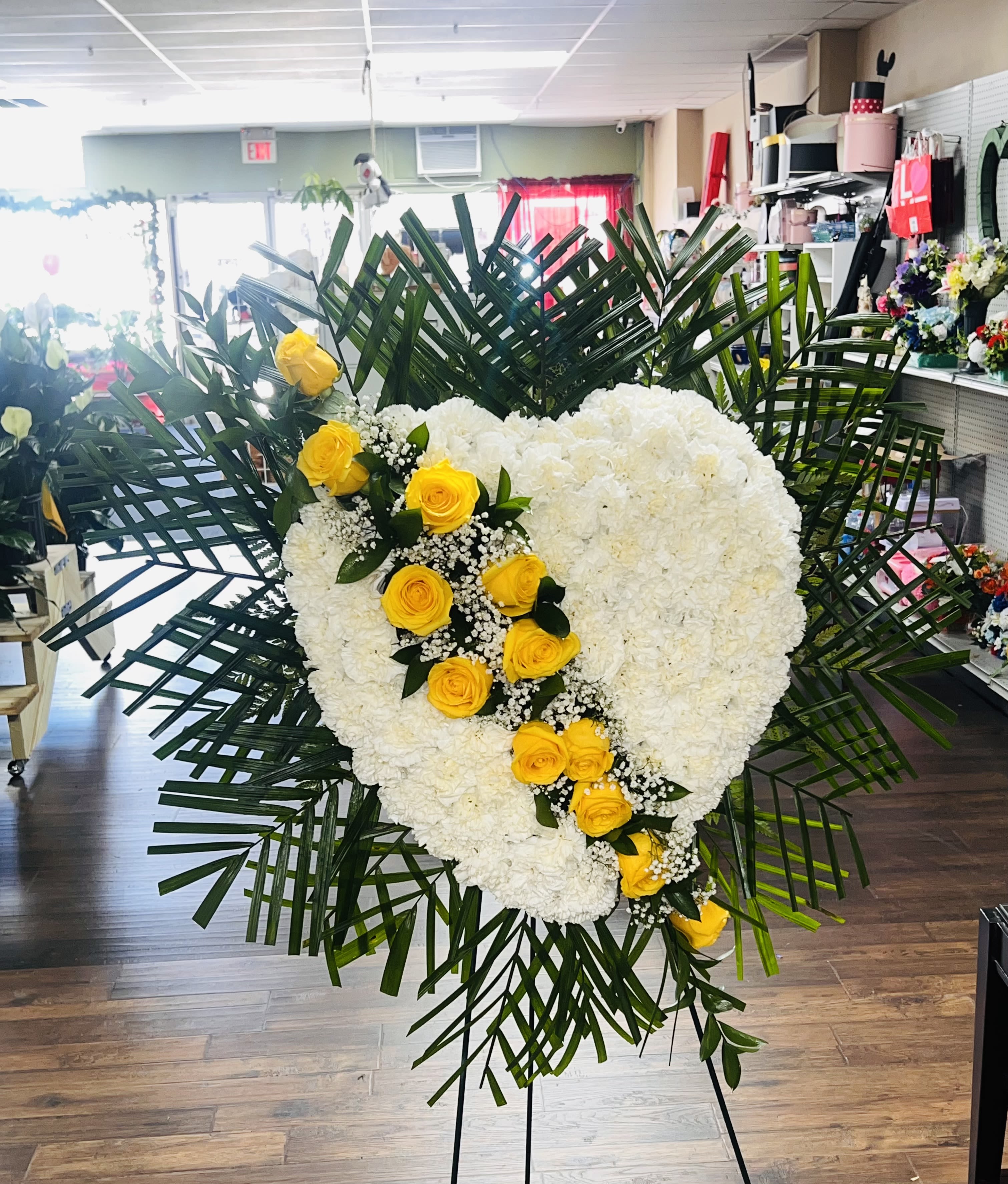 Heart-shaped white floral spray with yellow roses and palm fronds