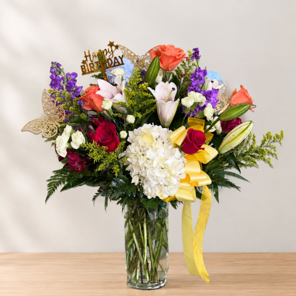 Mixed bouquet of roses, lilies, and hydrangea in a glass vase with a birthday topper