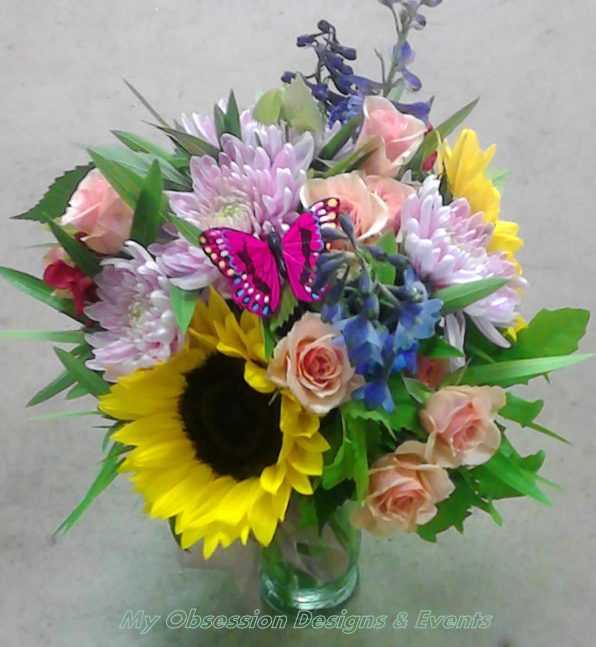 Mixed bouquet with sunflowers, roses, and purple blooms in a glass vase
