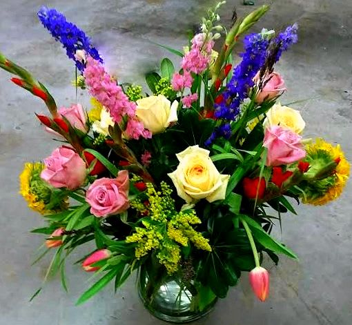 Mixed bouquet of roses and colorful tall blooms in a glass vase