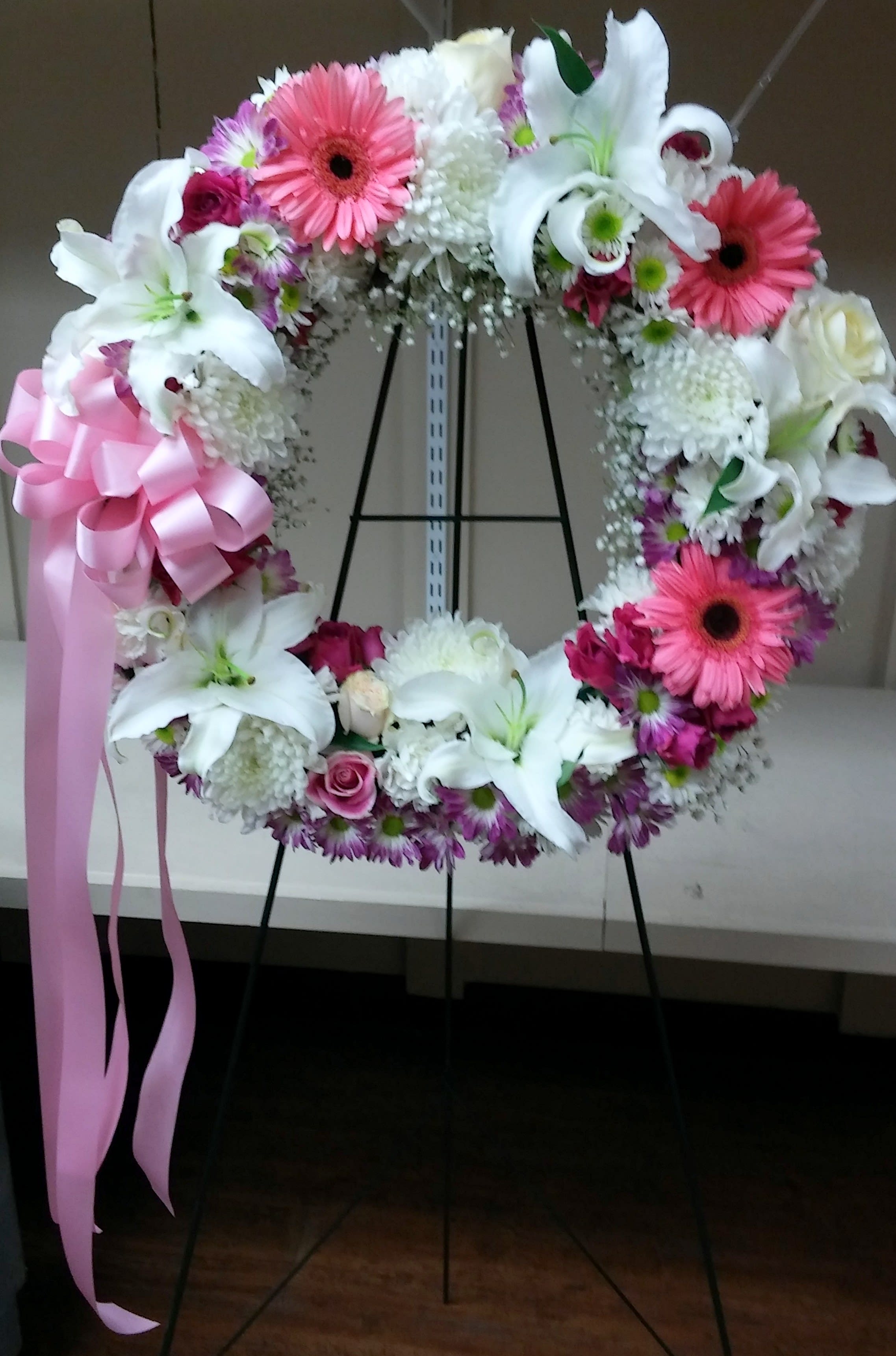 Floral wreath with white lilies, pink gerberas, and a pink ribbon bow