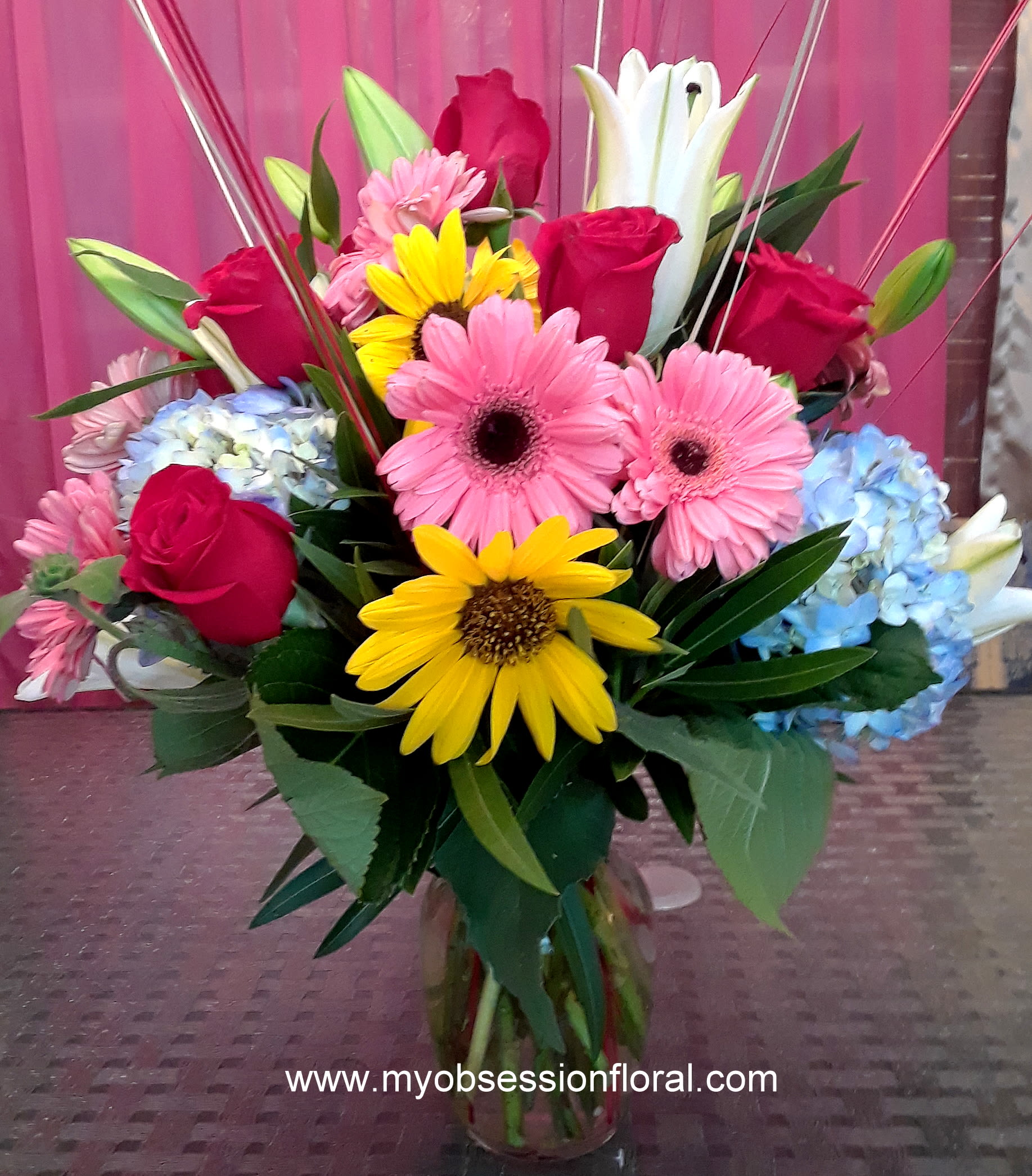 Mixed bouquet with roses, gerbera daisies, lilies, and hydrangeas in a glass vase