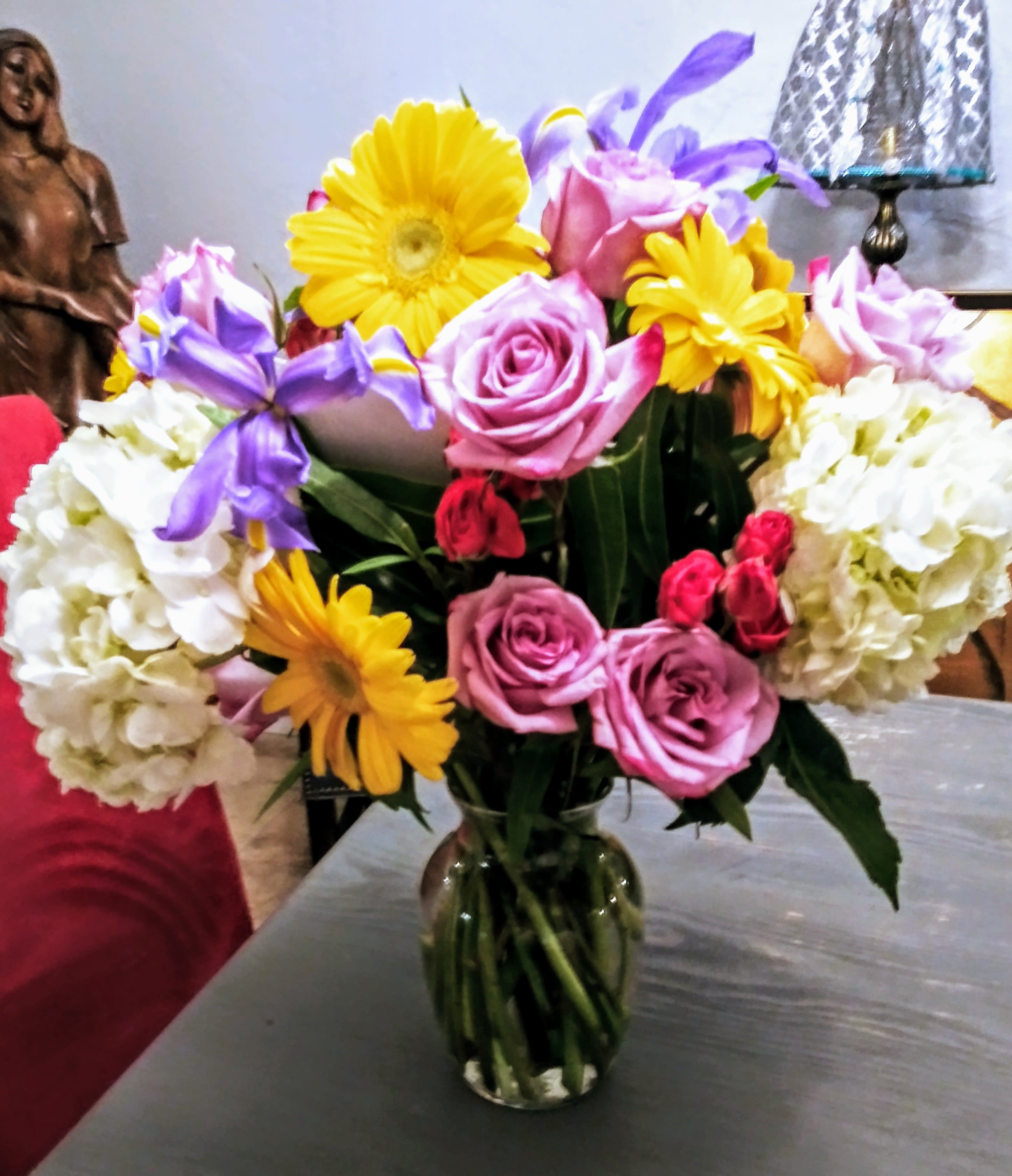 Bouquet of pink roses, yellow daisies, and white hydrangeas in a glass vase