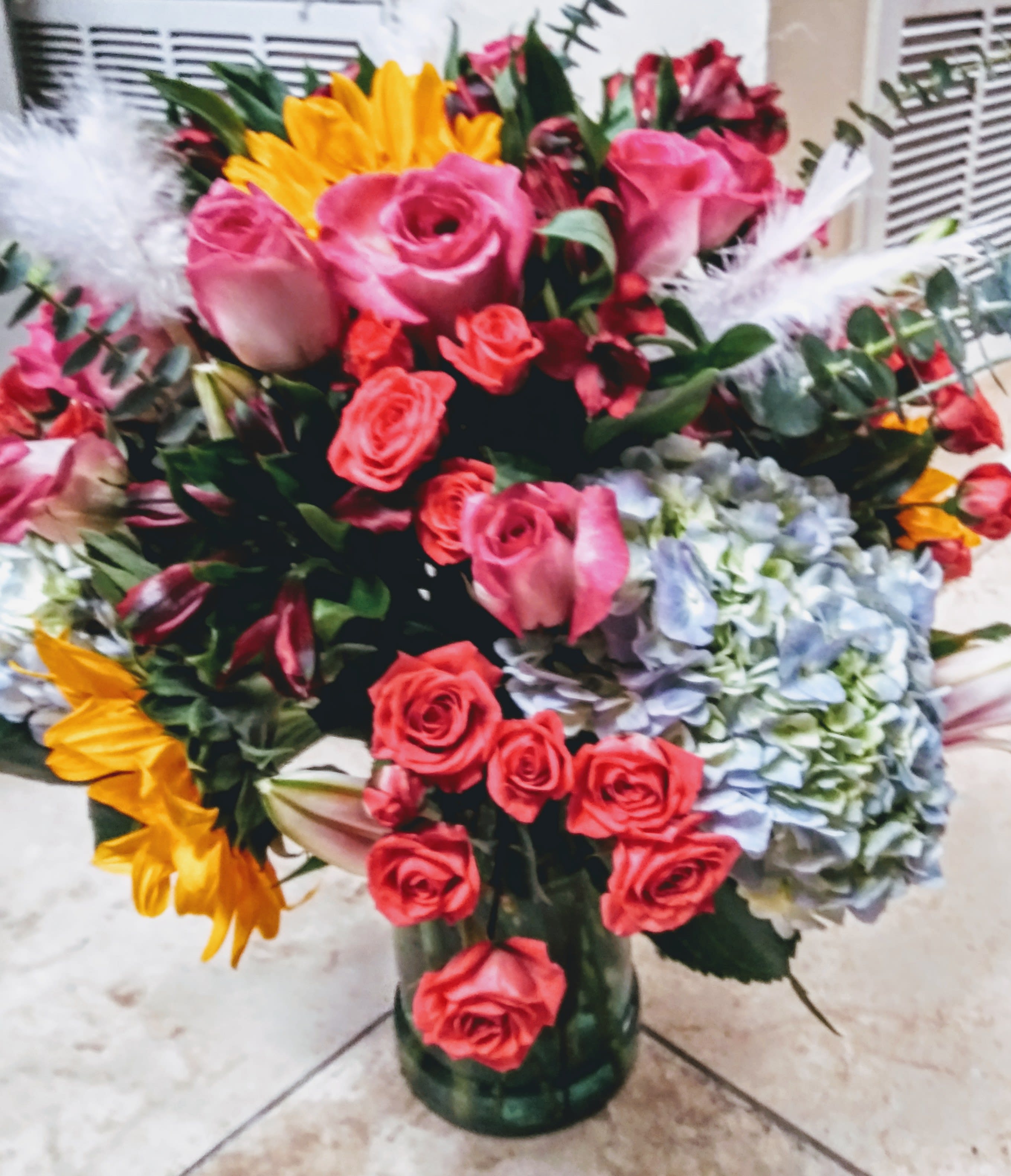 Bouquet of pink and red roses with sunflowers and hydrangeas in a glass vase