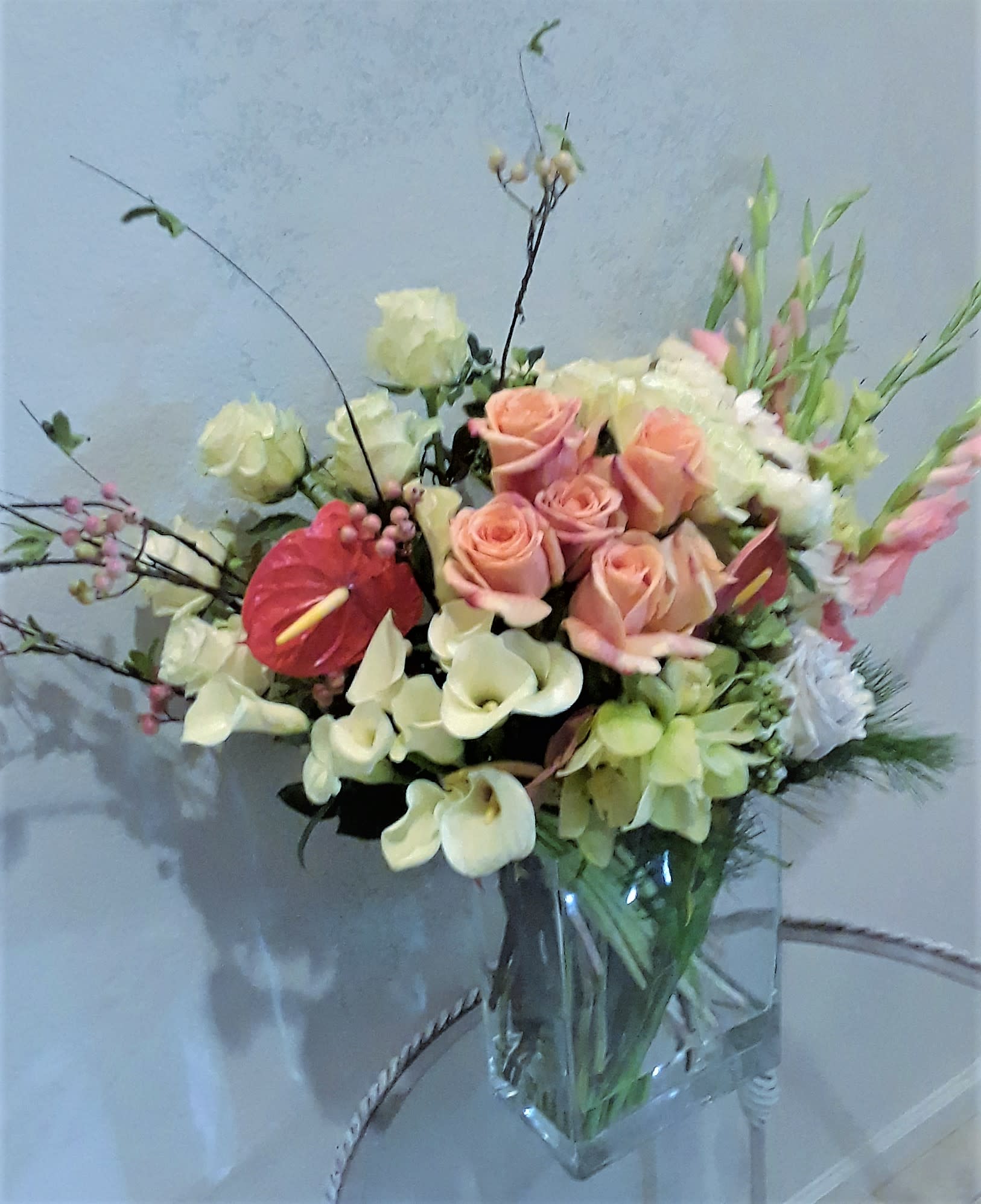 Mixed bouquet of peach roses, white calla lilies, and pink anthurium in a glass vase