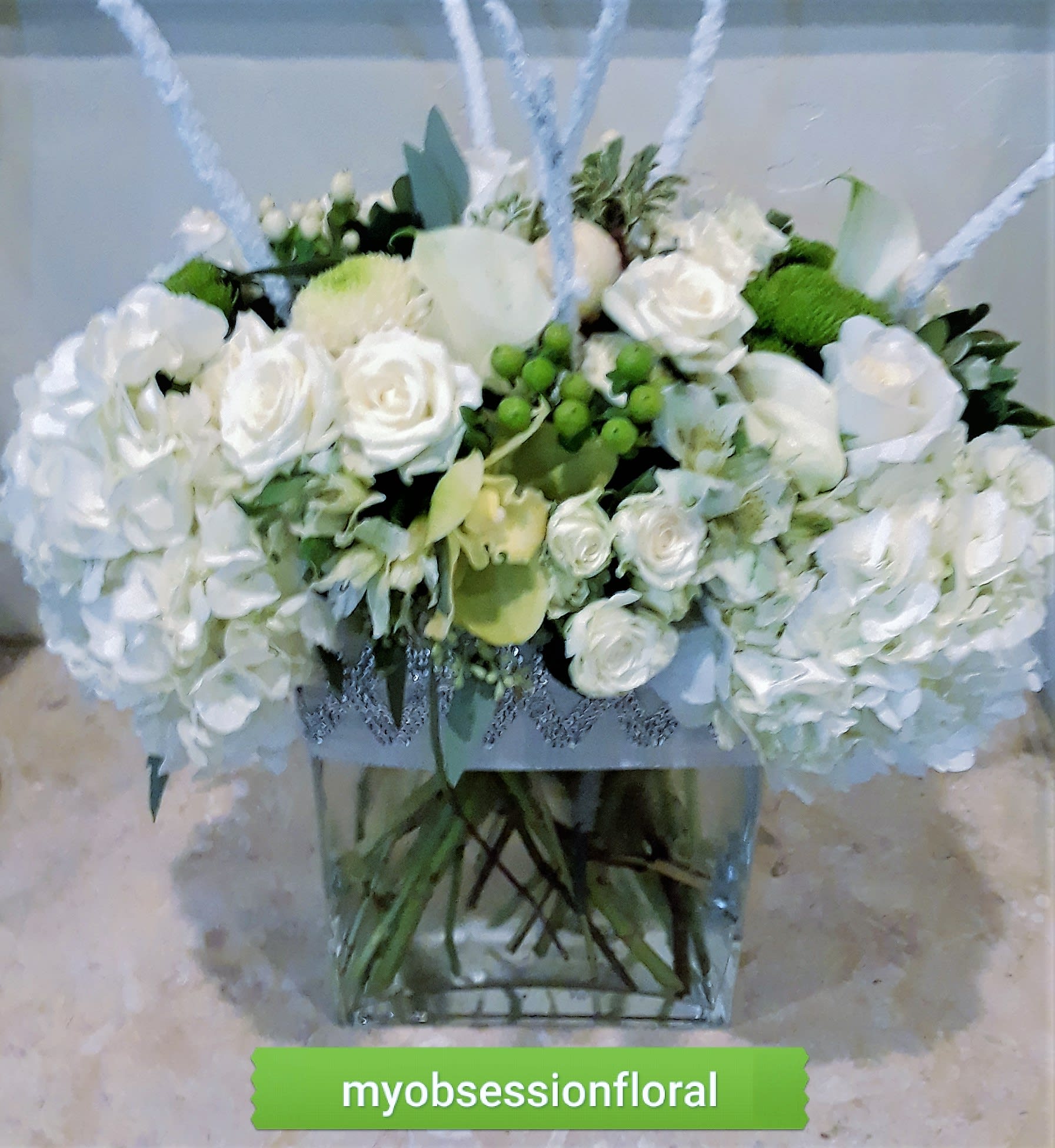 White rose arrangement in a clear square vase with green accents