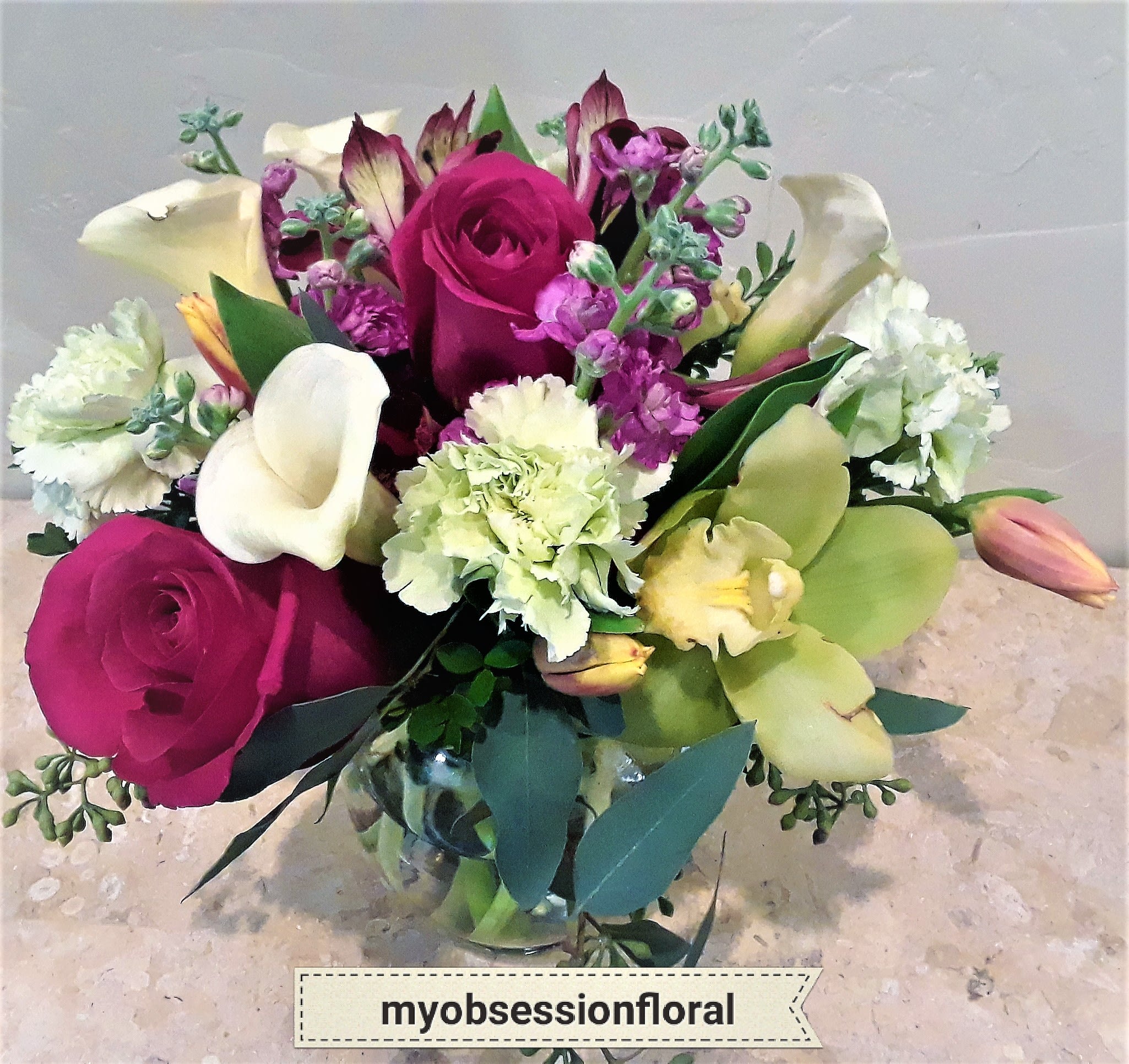 Bouquet of magenta roses, white calla lilies, and purple flowers in a glass vase