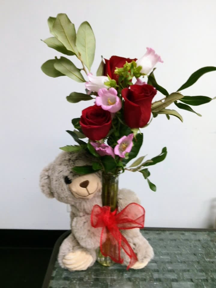 Red roses and pink flowers in a glass vase with a teddy bear
