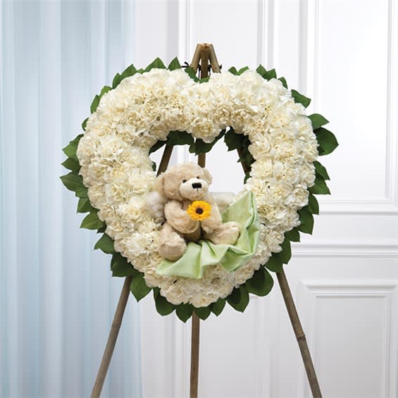Heart-shaped white floral wreath with a teddy bear and ribbon on an easel