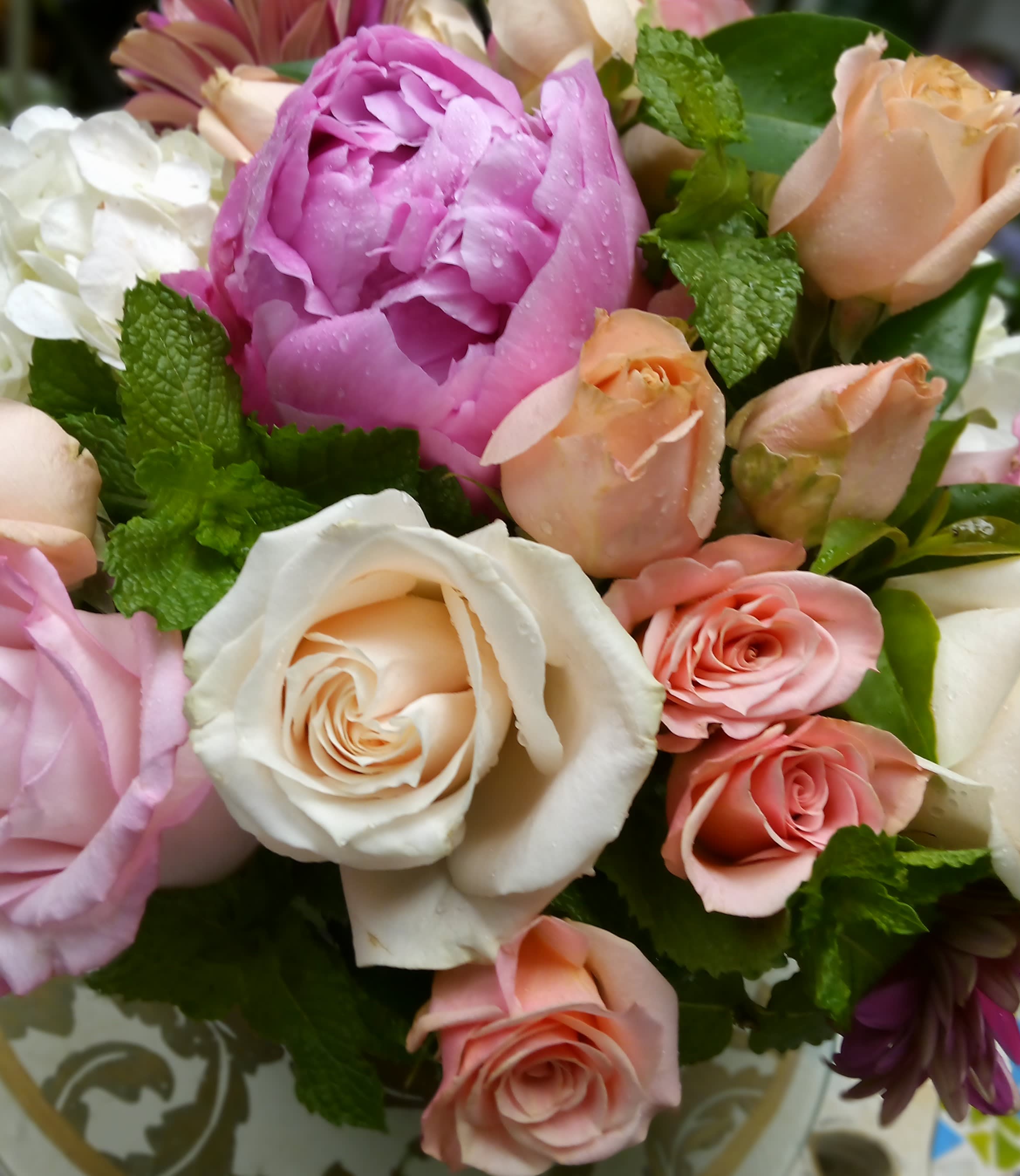 Mixed bouquet of pink, peach, and white roses with a large pink peony