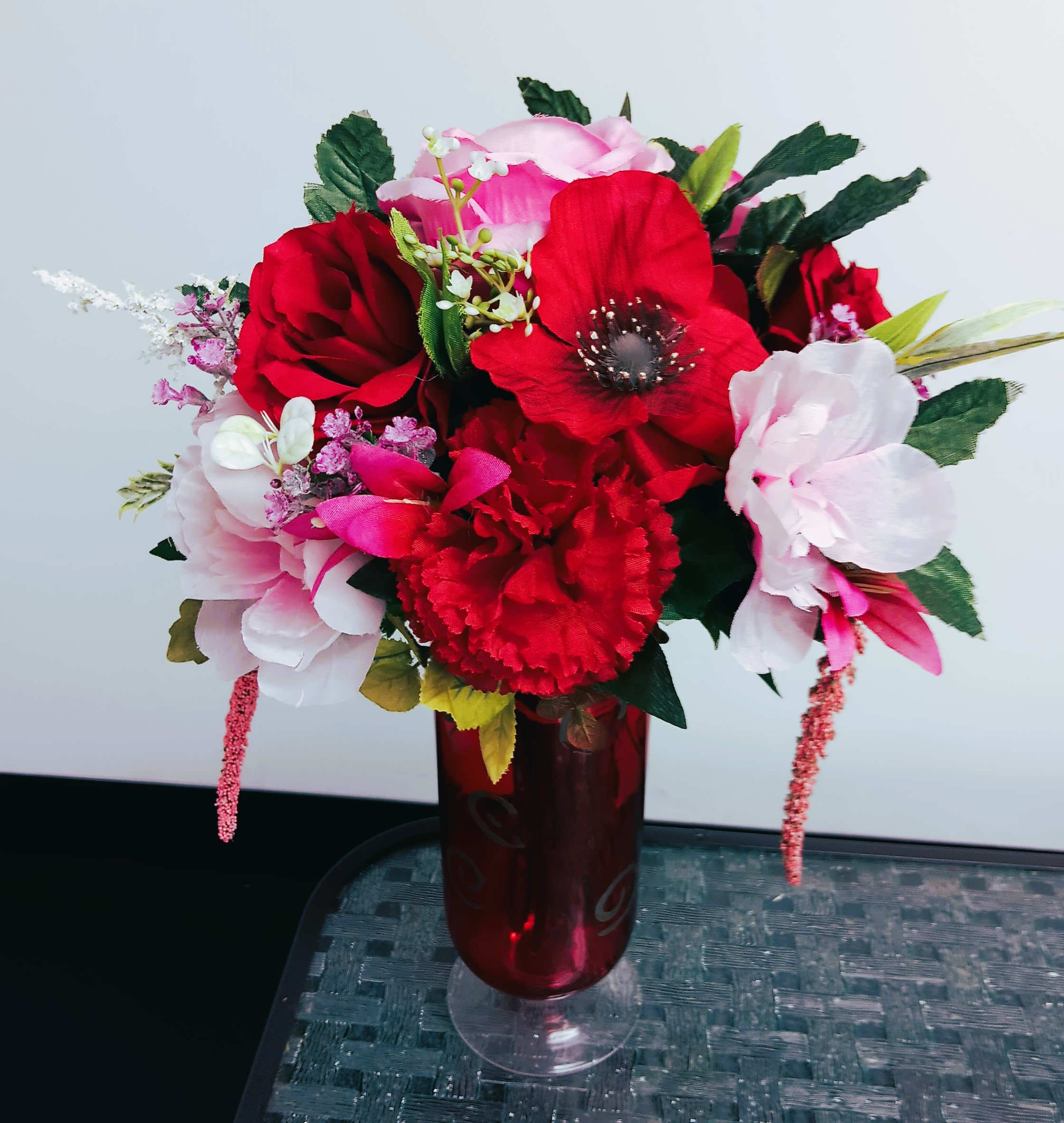 Red and pink floral arrangement in a red glass vase