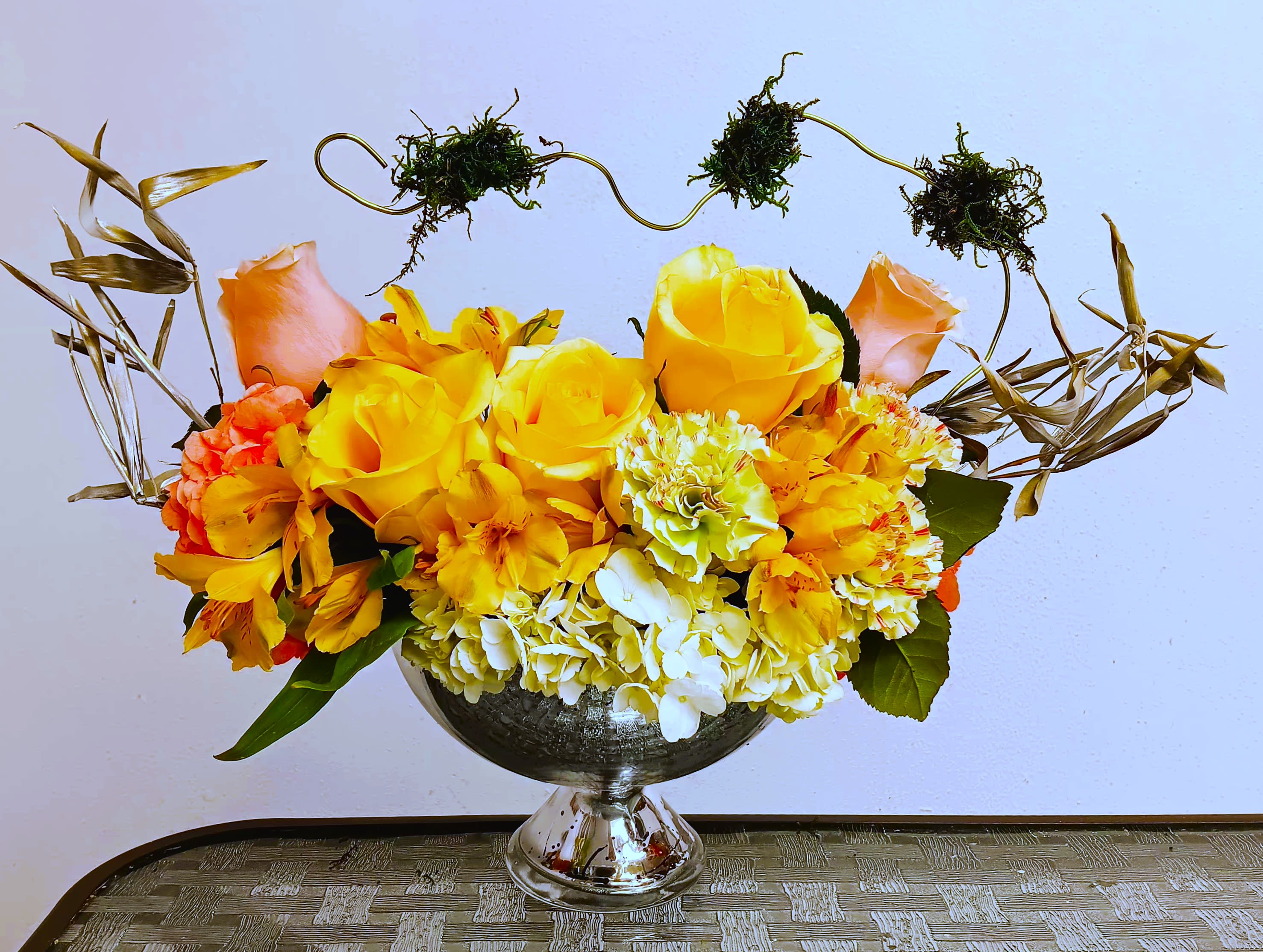 Yellow and orange flower arrangement in a silver pedestal vase