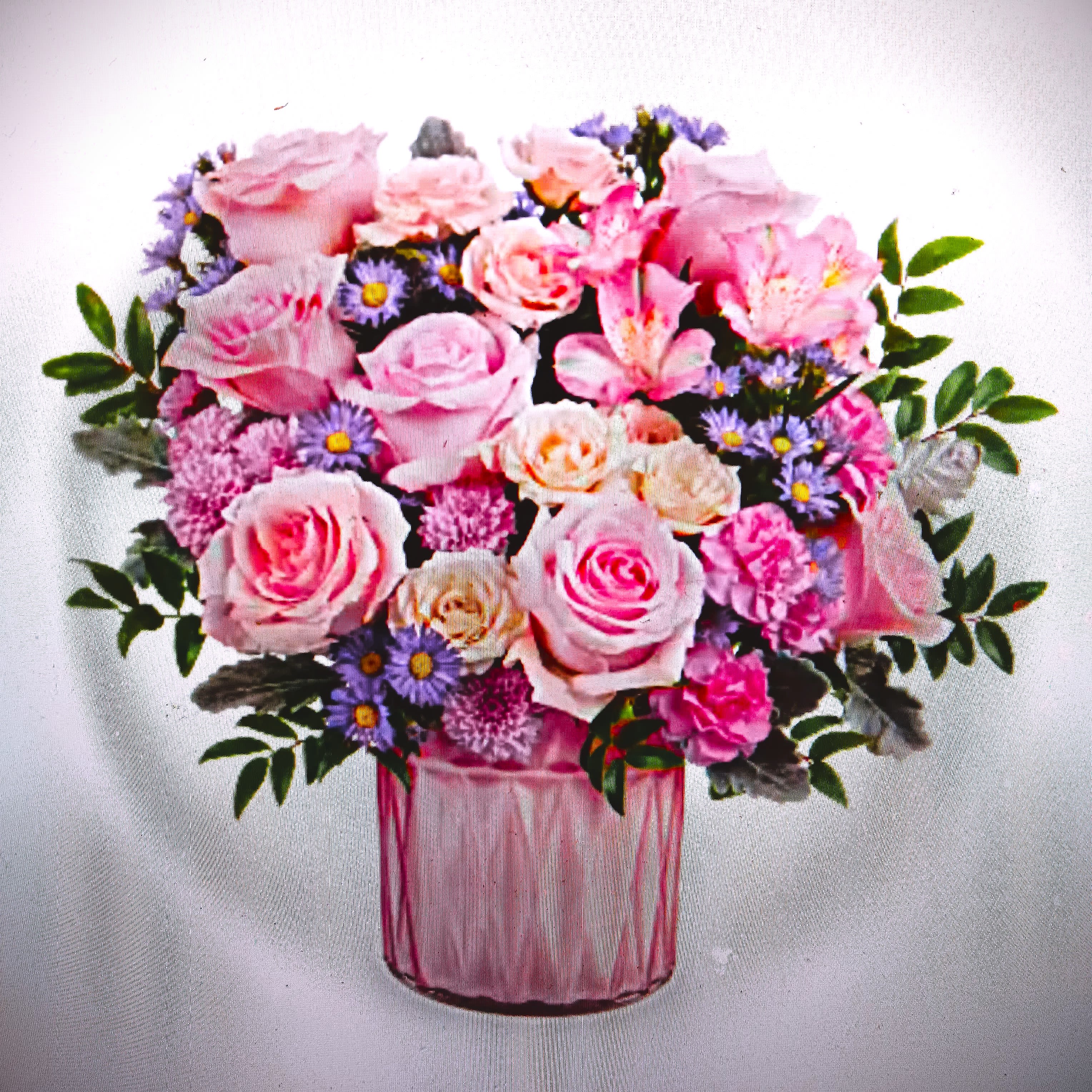 Pink and cream rose arrangement with lavender filler flowers in a pink glass vase