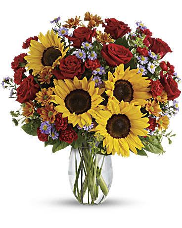 Bouquet of sunflowers, red roses, and small purple flowers in a glass vase