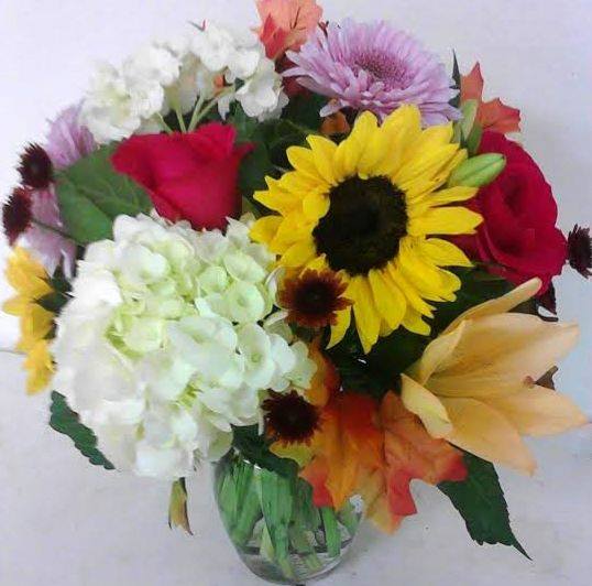 Mixed bouquet with sunflowers, roses, hydrangeas, and lilies in a glass vase