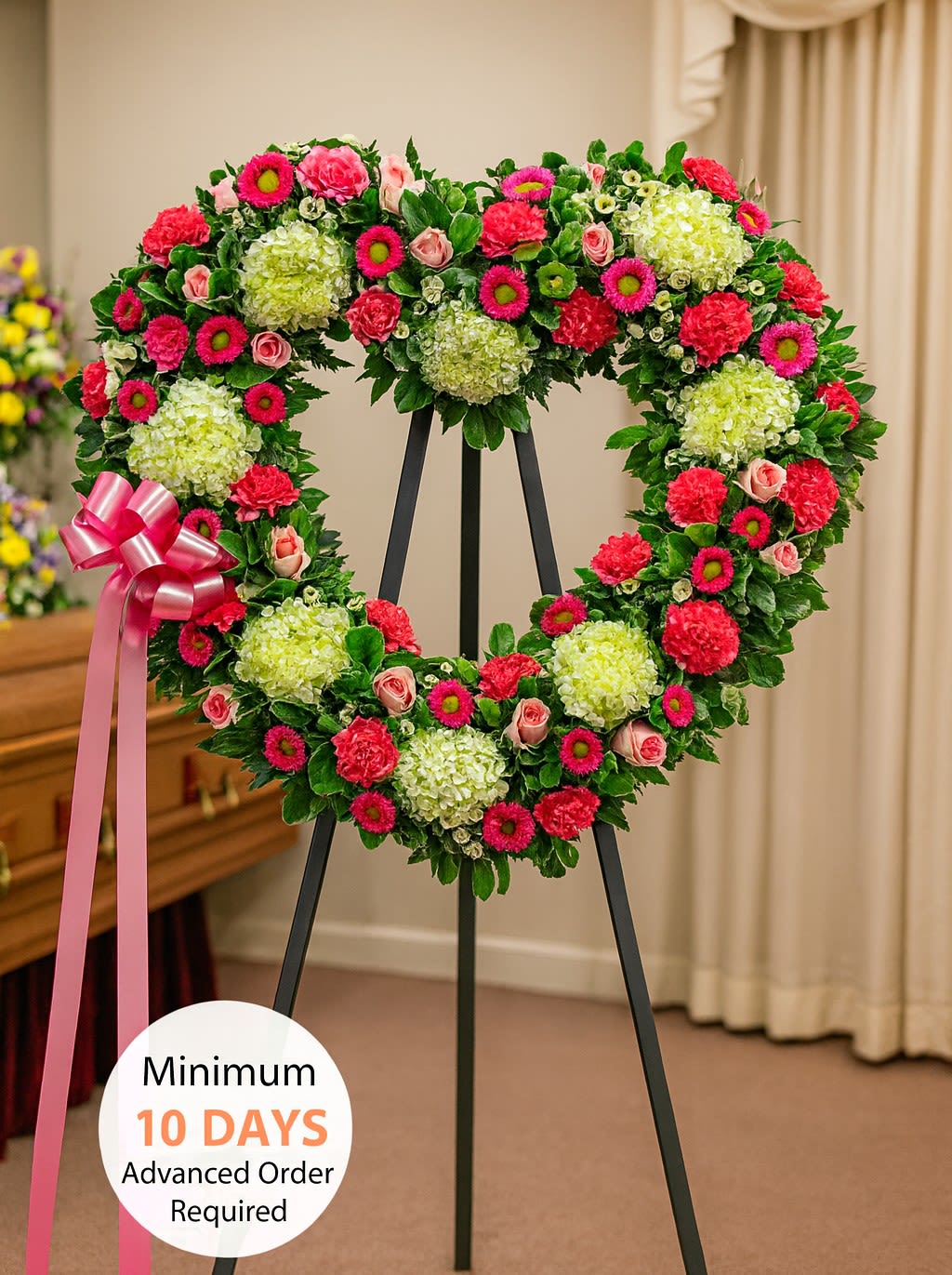 Heart-shaped standing wreath with green hydrangeas, pink roses, and bright pink flowers on a black easel.