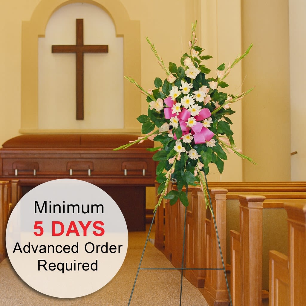Standing spray of white and pink flowers with a pink bow on an easel in a church