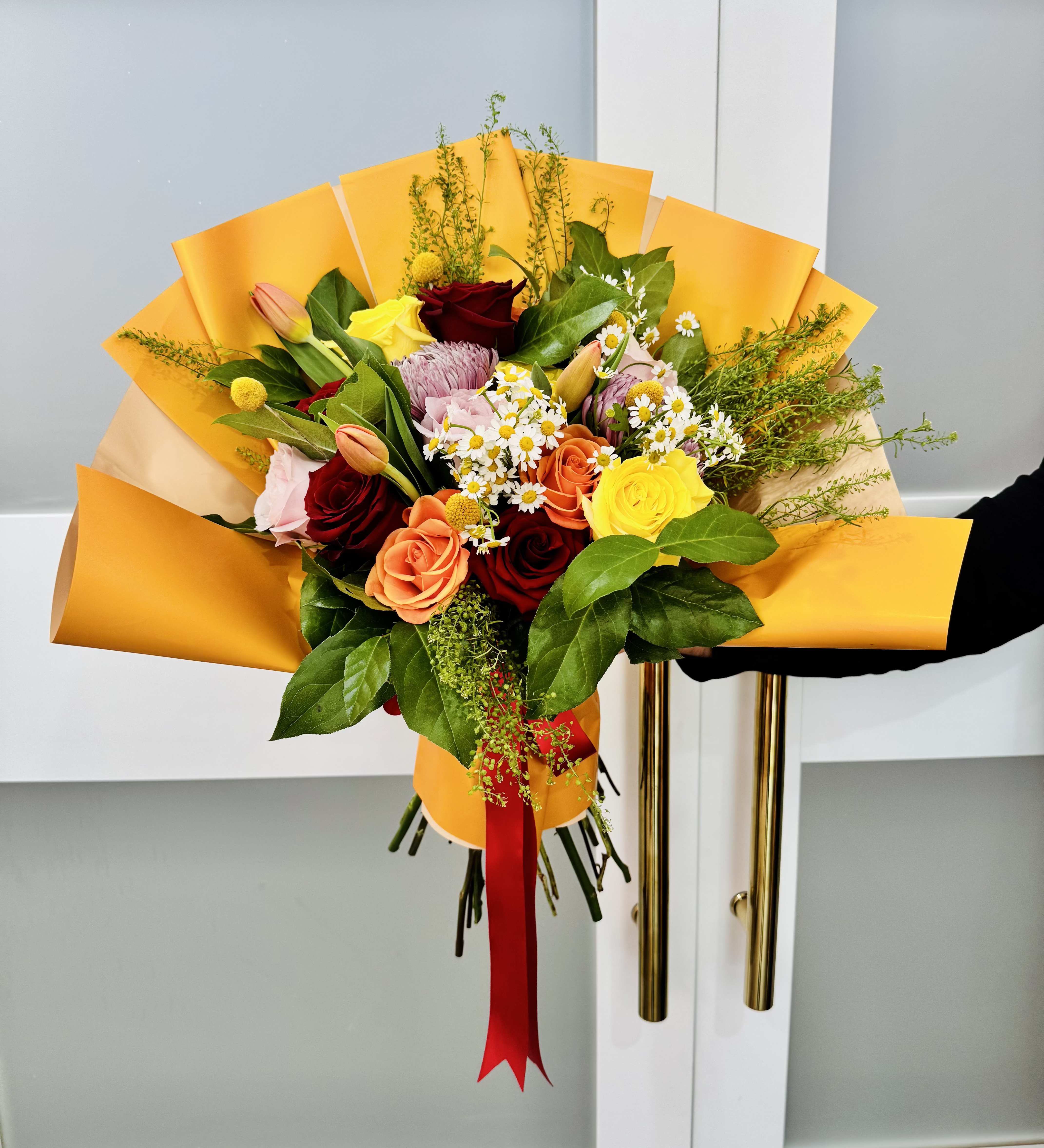 Hand-tied bouquet of mixed roses and small daisies wrapped in yellow paper