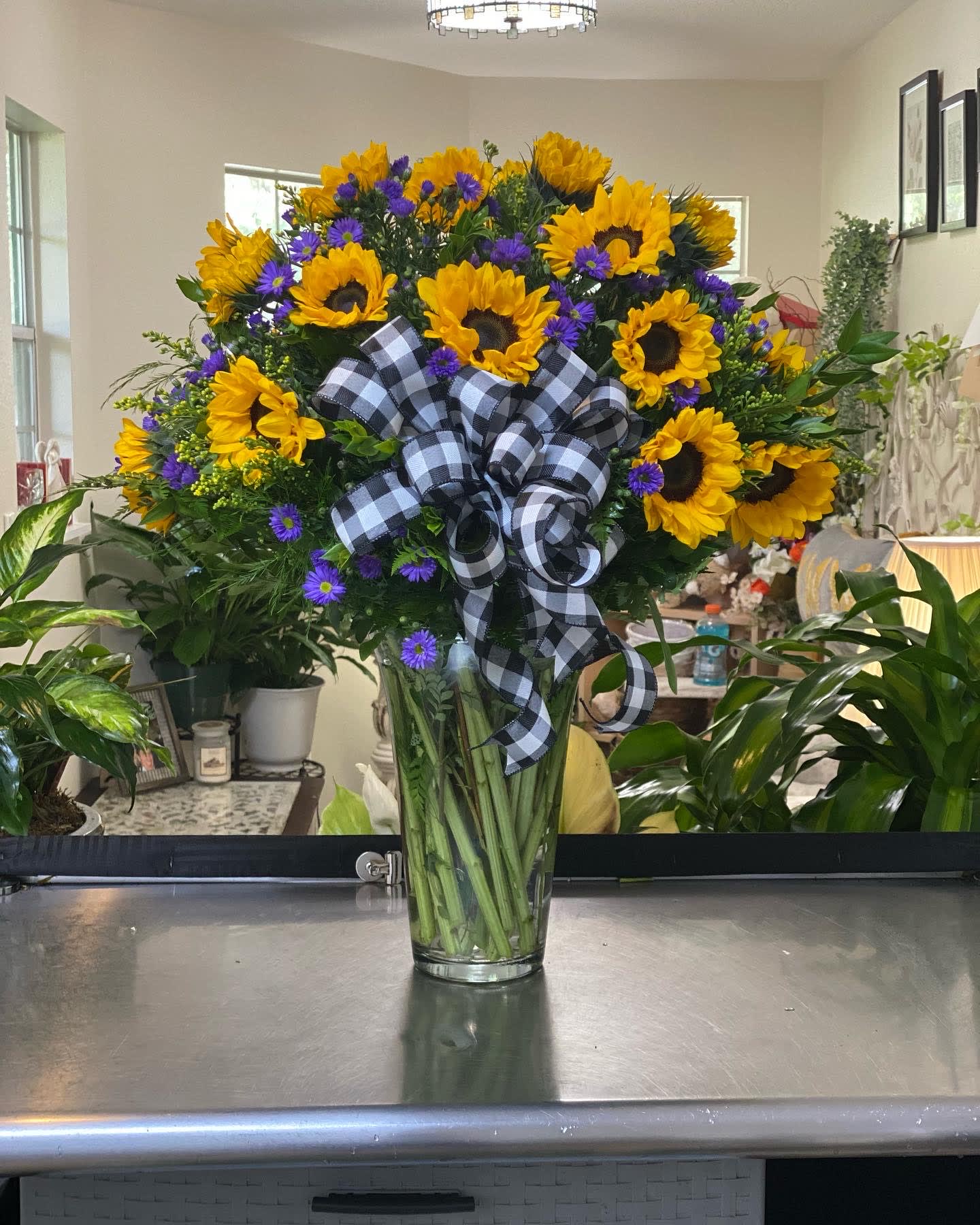 Sunflower bouquet with purple daisies in a clear glass vase and plaid ribbon