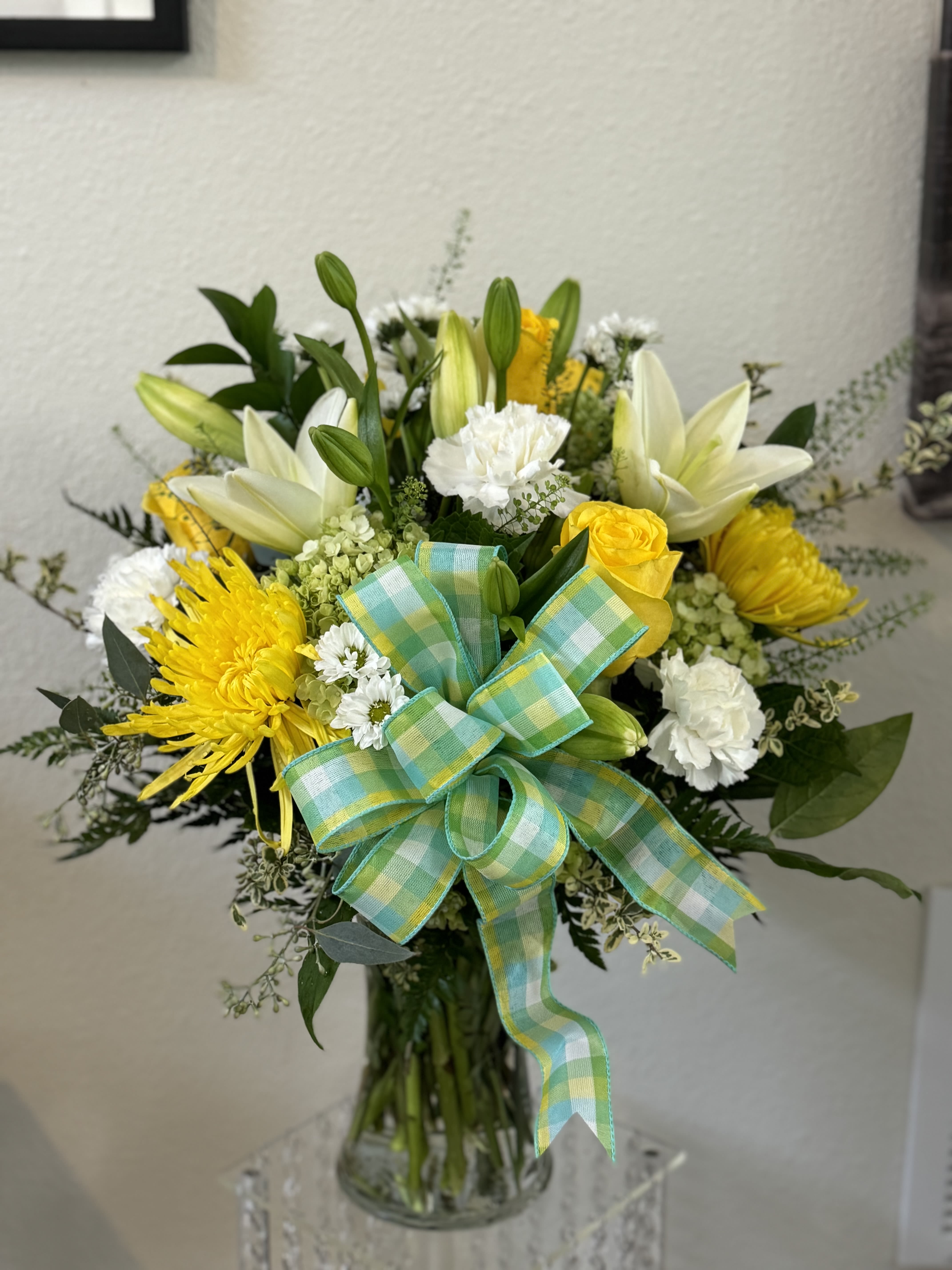 Yellow and white flower bouquet in a glass vase with a plaid ribbon