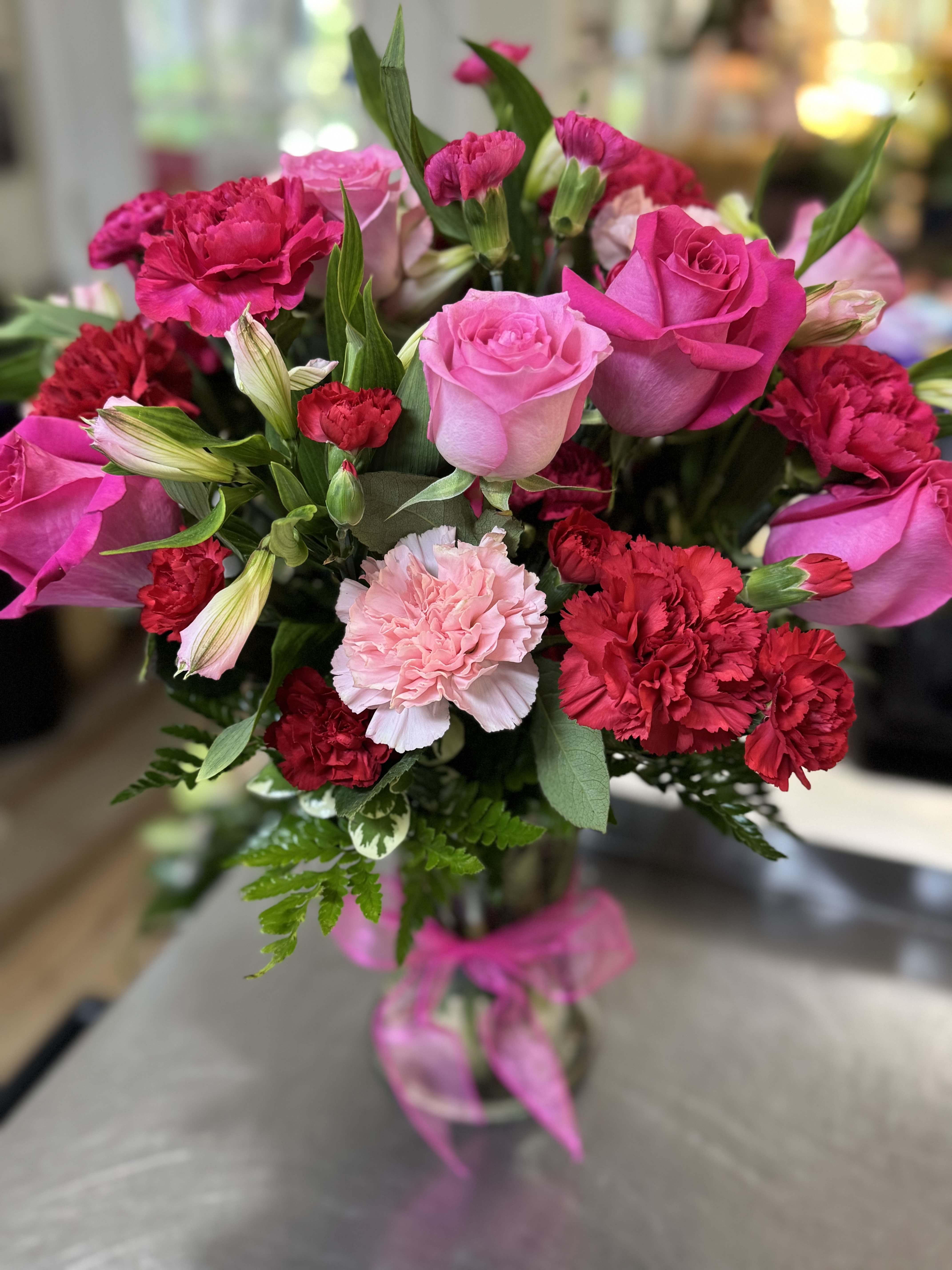Pink roses and red carnations in a glass vase with a pink ribbon