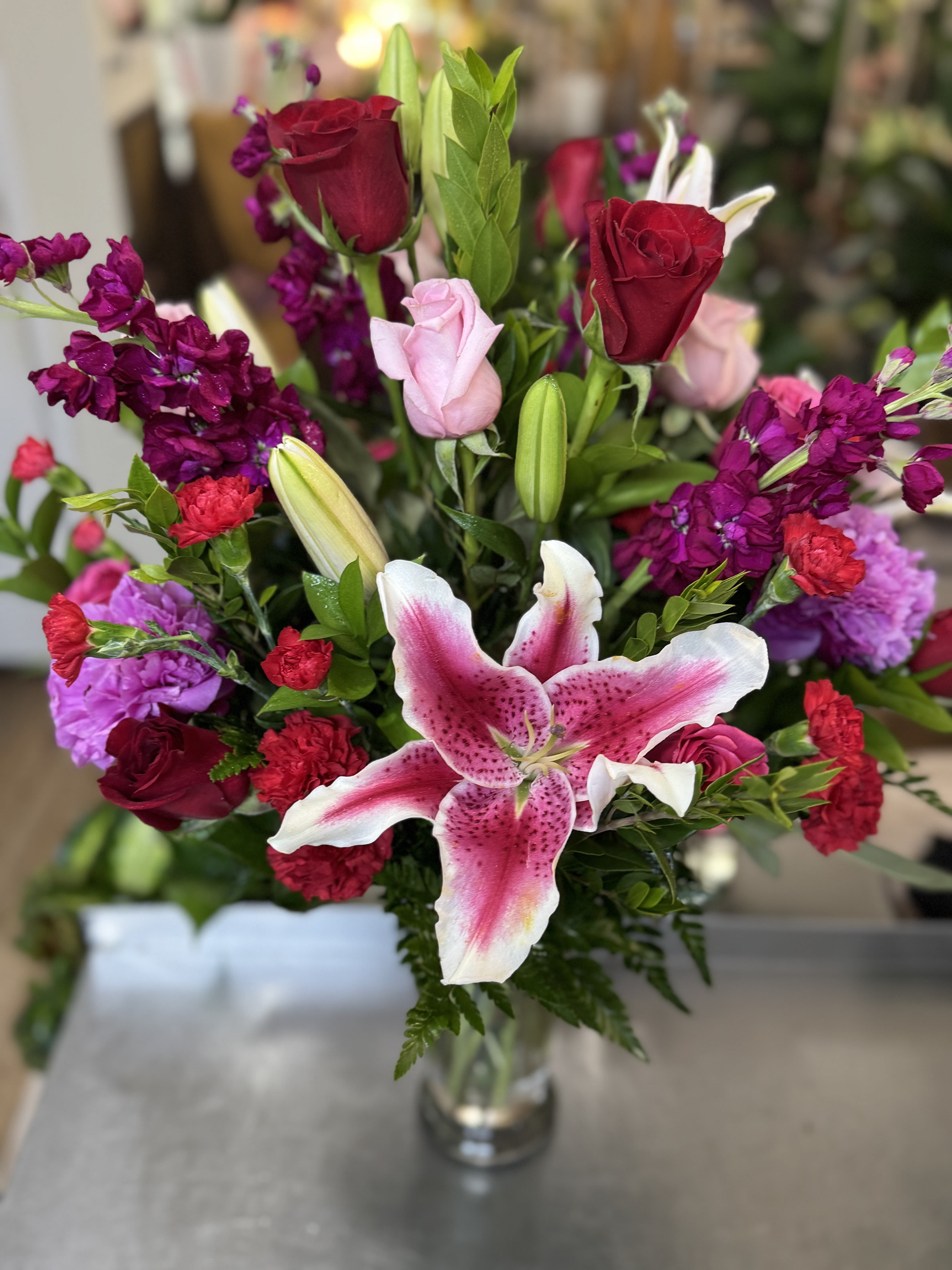 Bouquet of pink lilies, red roses, and purple flowers in a glass vase