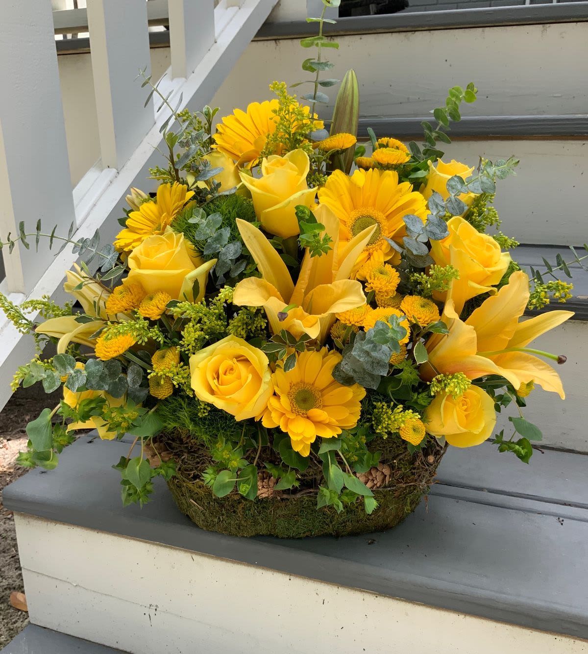 Elite Garden - A bright and elegant arrangement designed in a natural basket, featuring open yellow lilies, fresh yellow roses, and fragrant eucalyptus accents. The blend of textures and golden tones creates a warm, cheerful design full of positive energy. Perfect for brightening any space, celebrating a milestone, or sending joy and appreciation.