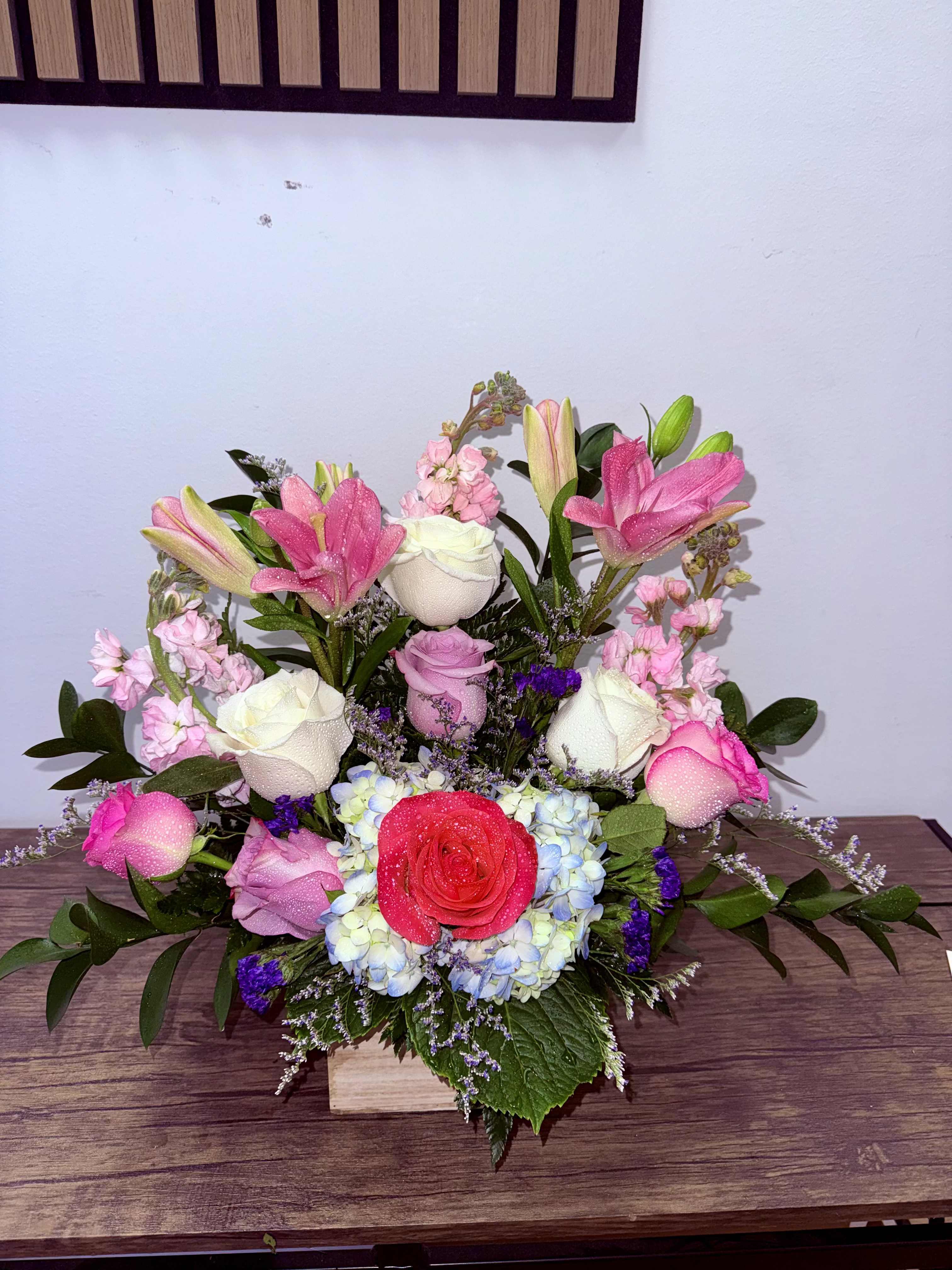 Lush Ligth - A fresh and elegant arrangement featuring white roses, pink lilies, and complementary blooms, beautifully designed in a natural wooden base. Ideal for any special occasion.